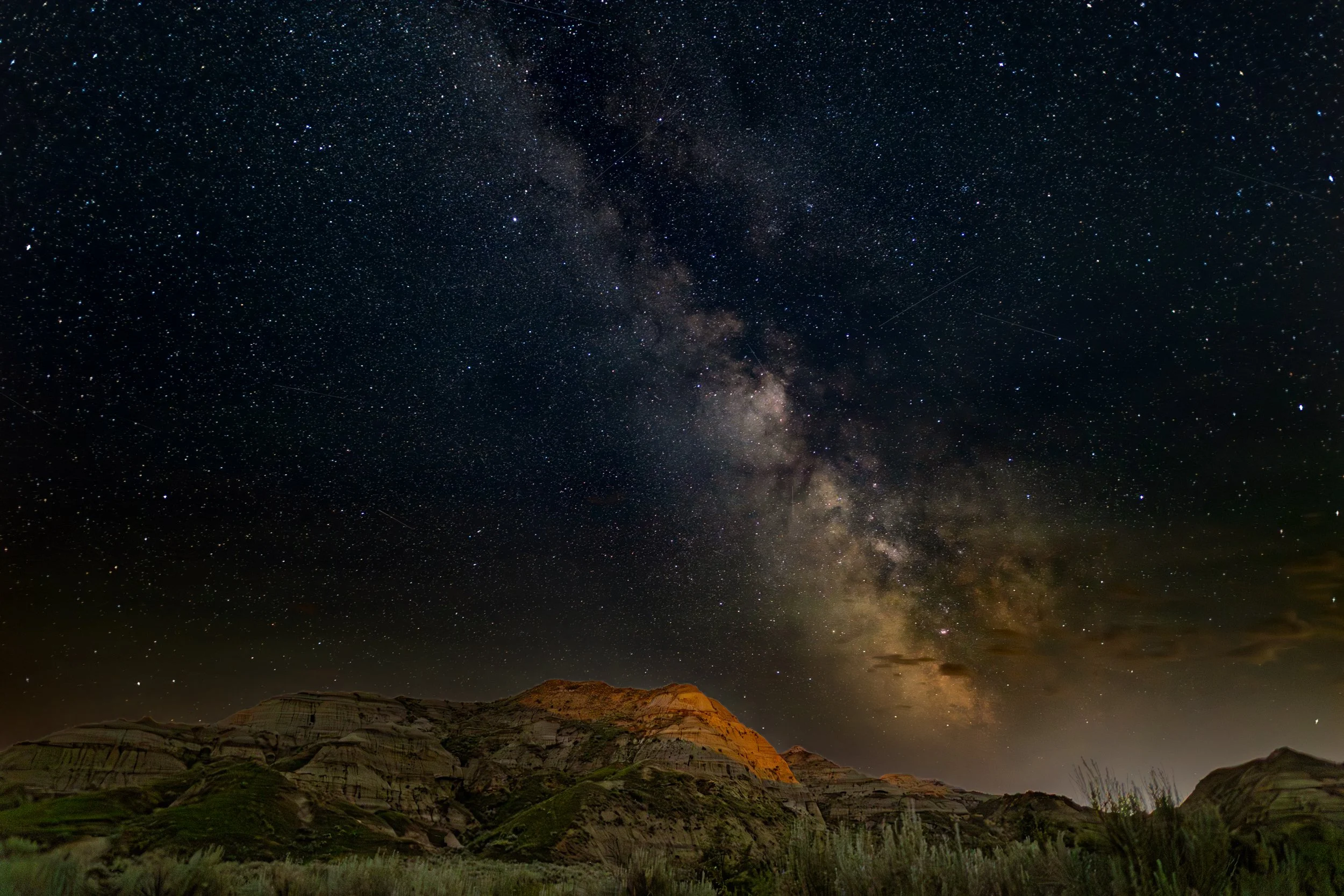 A night sky filled with stars and the Milky Way galaxy, with a silhouette of rugged hills or mountains in the foreground.