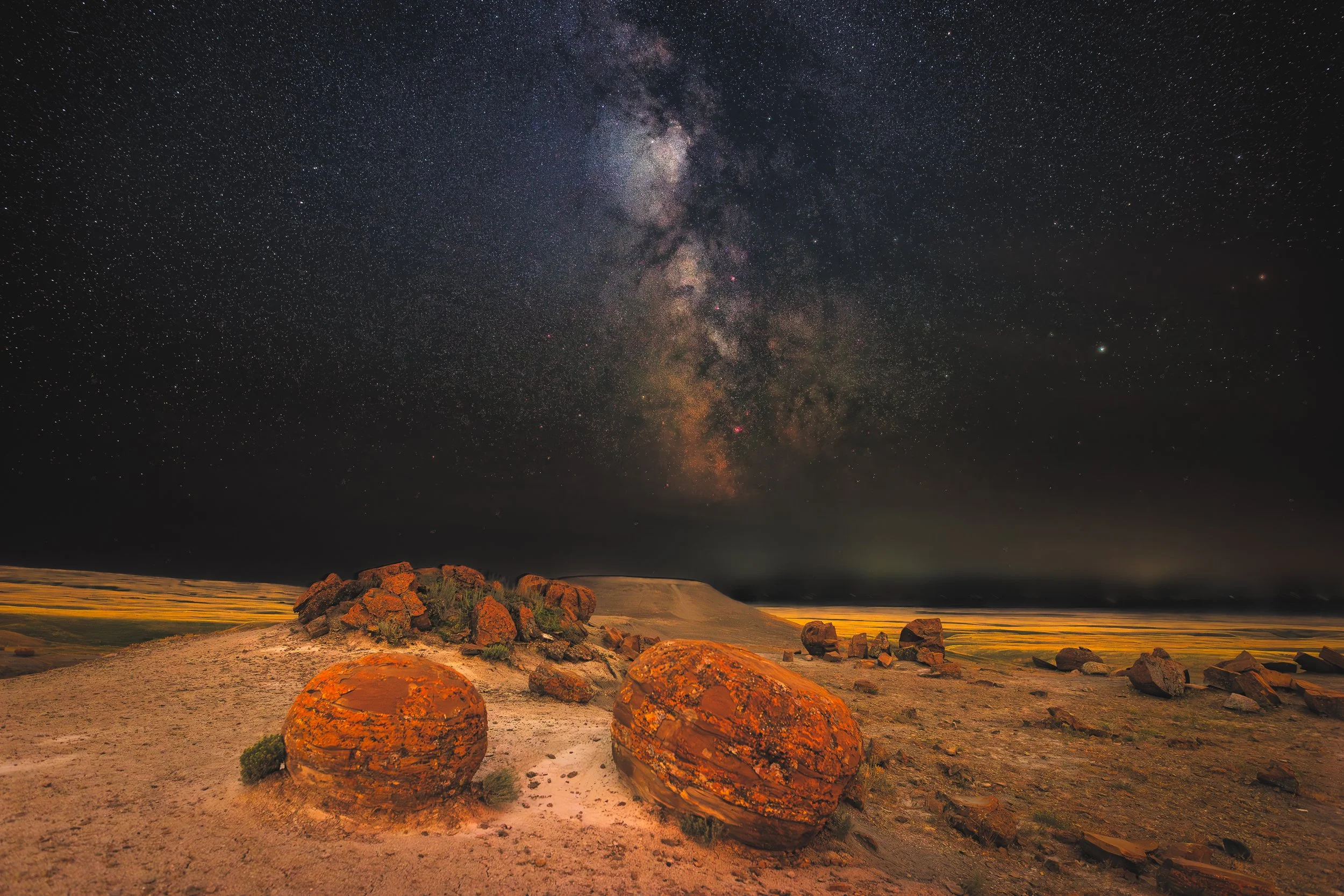 Night sky with the Milky Way galaxy over a desert landscape with scattered rocks.