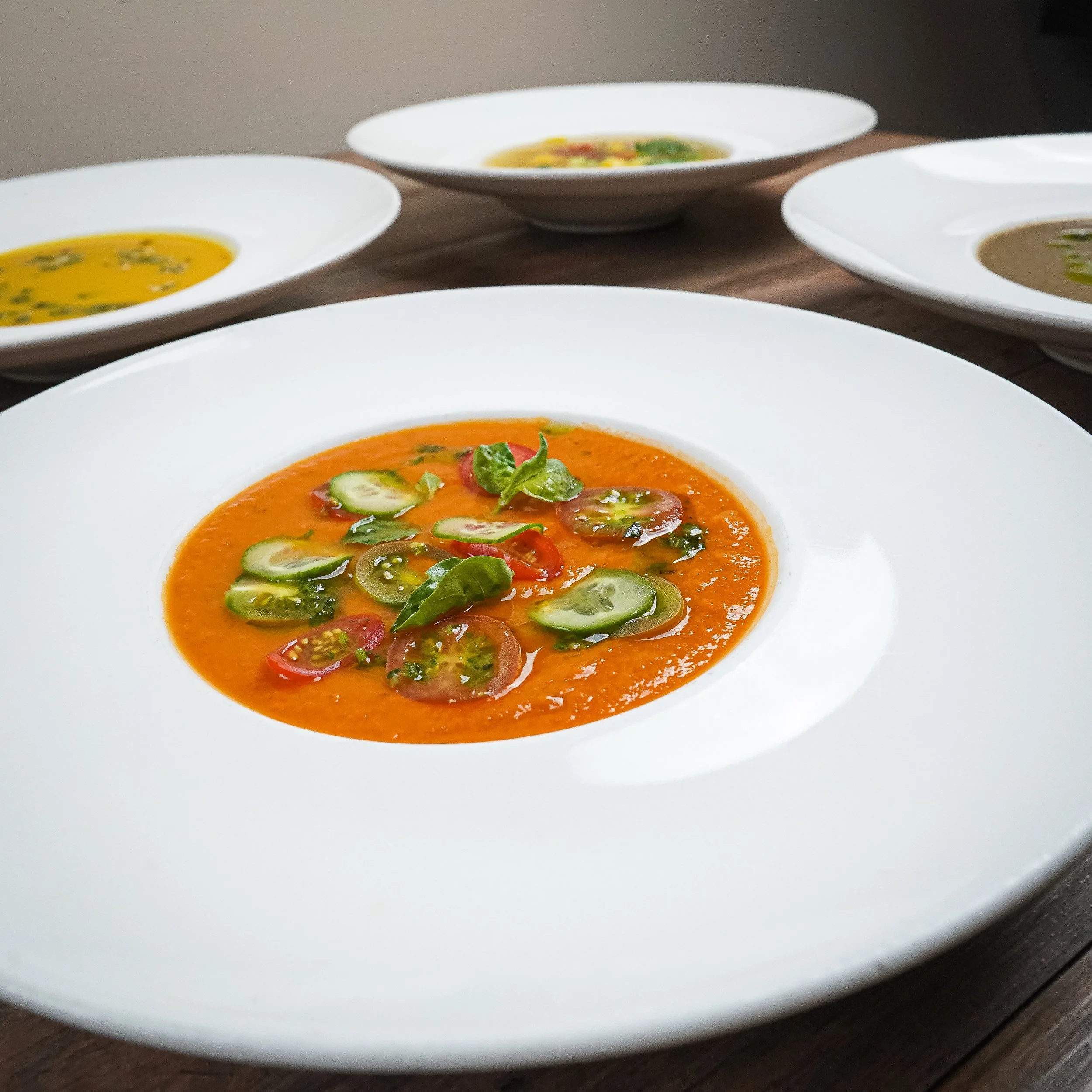 A white plate with tomato and cucumber salad in orange sauce, garnished with fresh basil leaves.