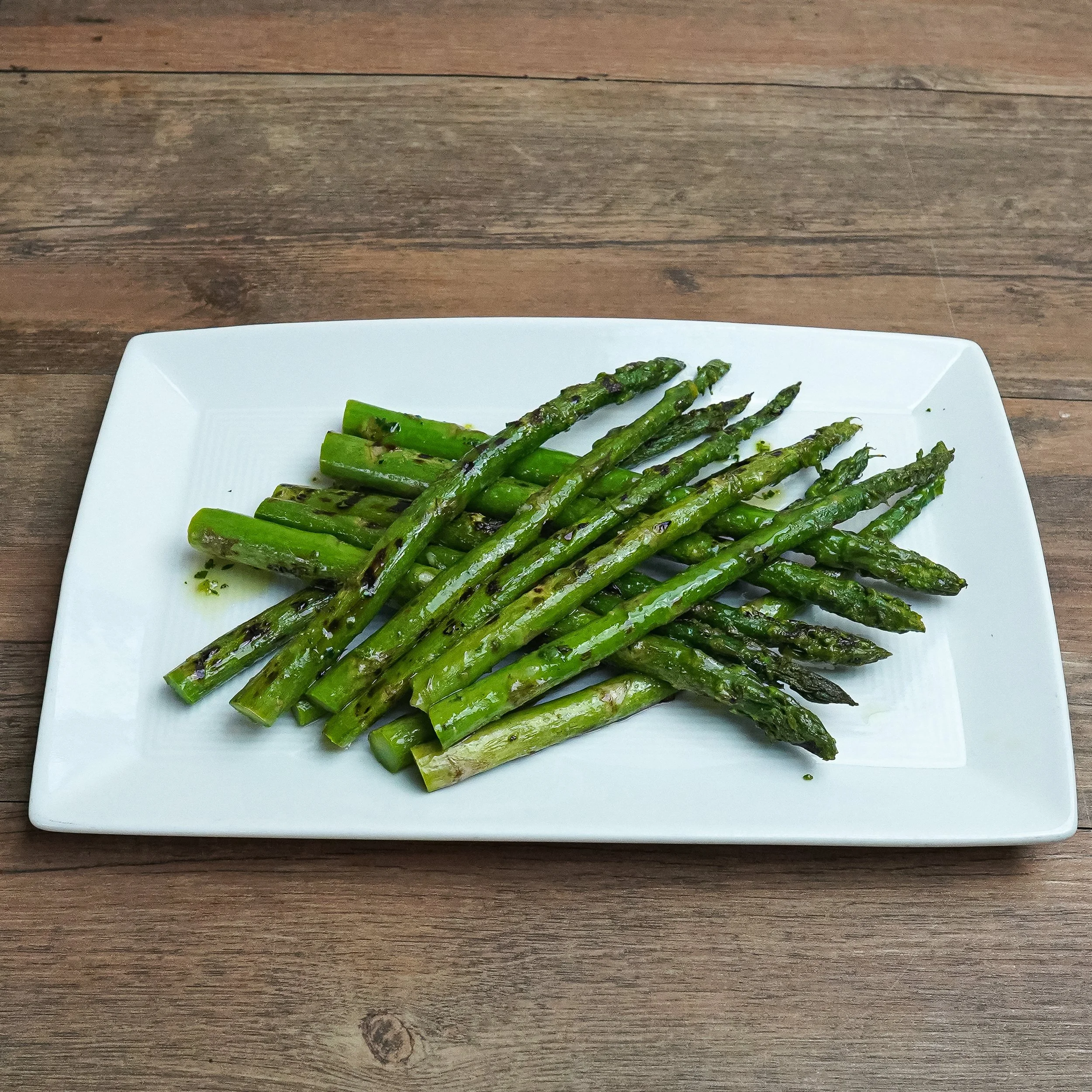Grilled asparagus on a white rectangular plate placed on a wooden table.