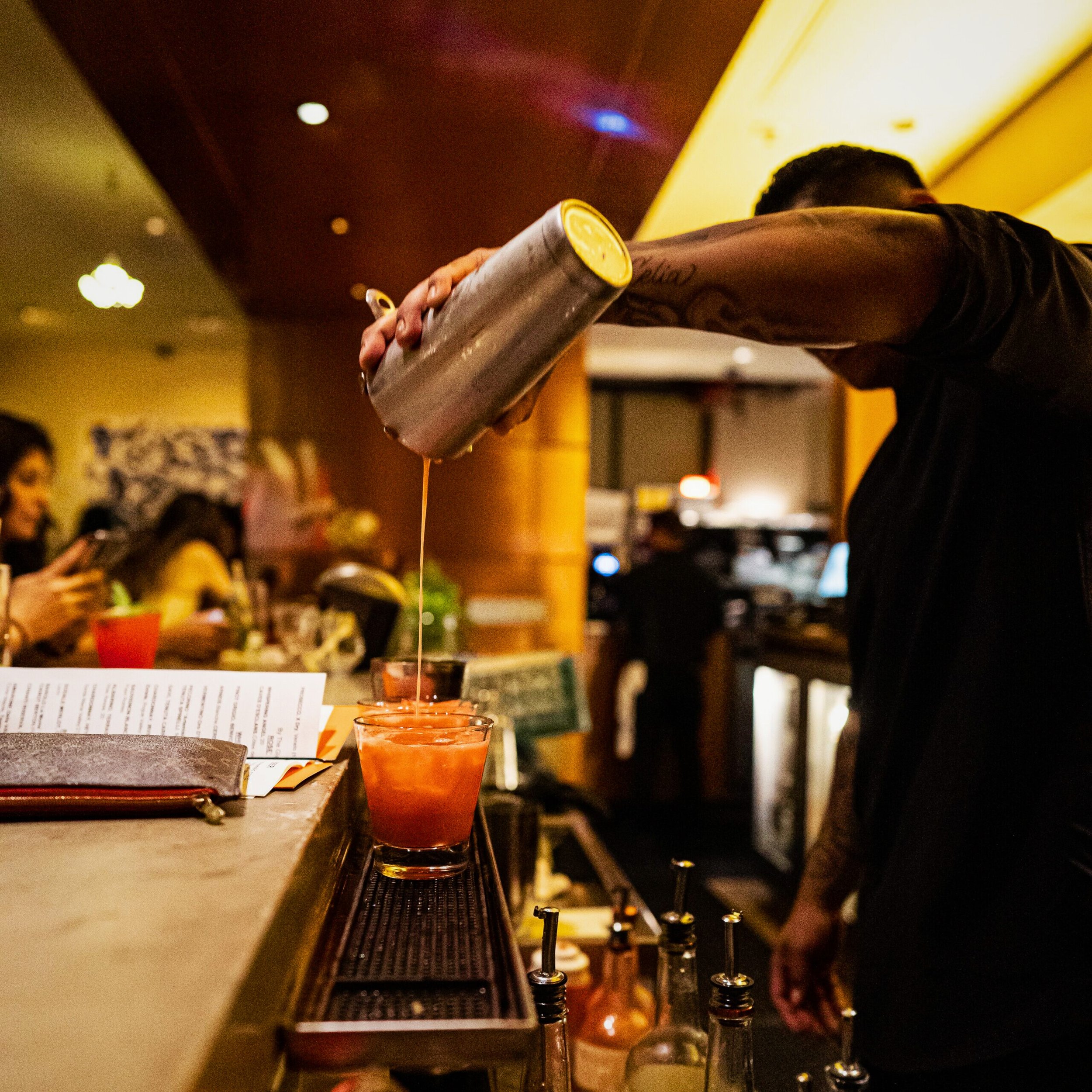 Bartender pouring a cocktail into a glass at a bar.