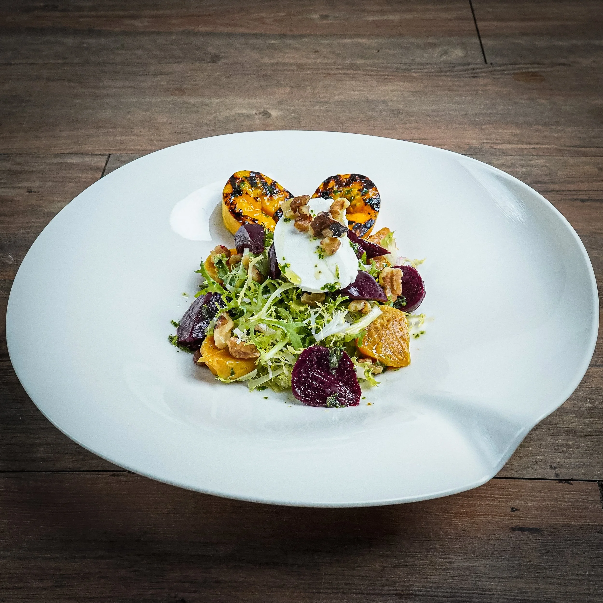 Salad with roasted squash, beets, greens, nuts, and a dollop of sour cream on a white plate.