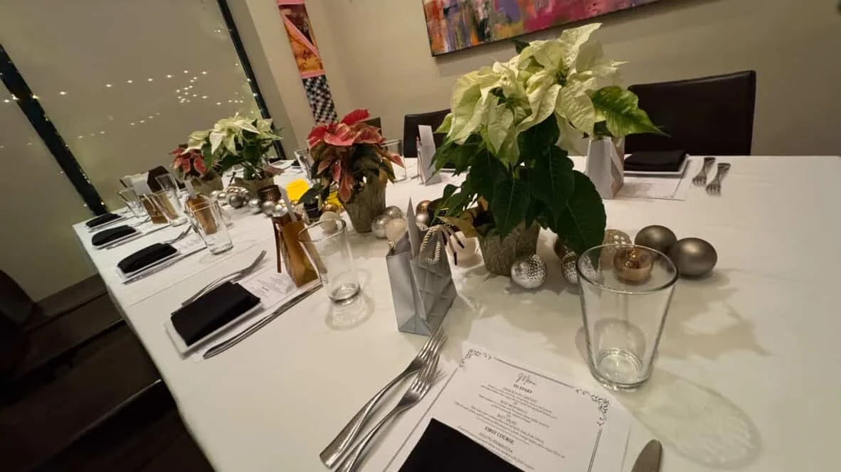 A decorated dining table with poinsettia plants, silver ornaments, candles, and a menu, set for a holiday dinner or celebration.