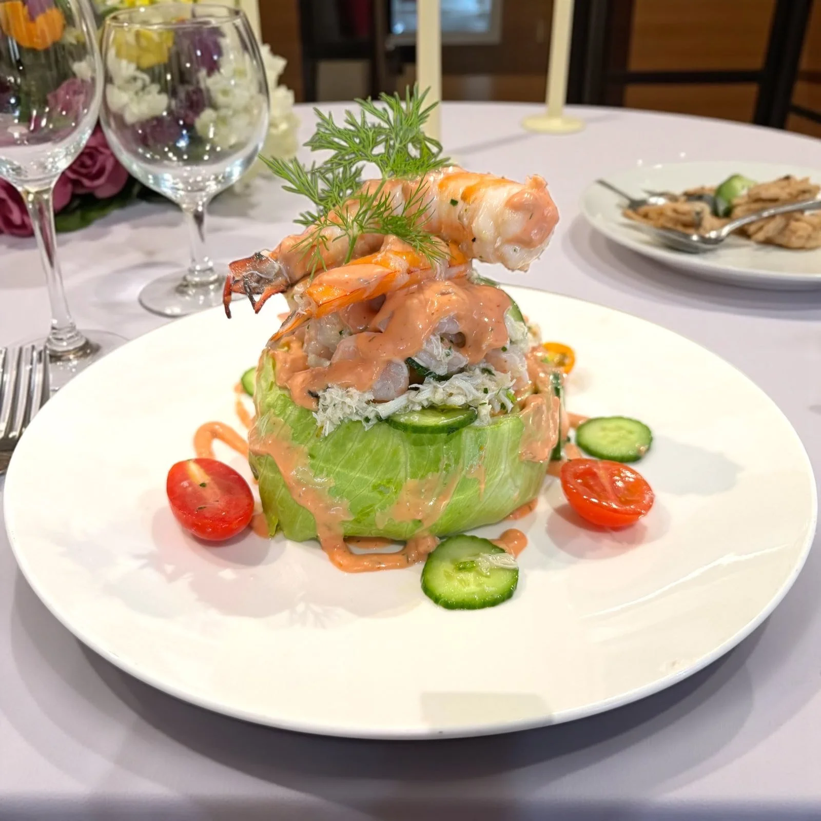 Lobster and seafood salad served inside a hollowed-out lettuce leaf, topped with dill, and garnished with cherry tomatoes and cucumber slices.
