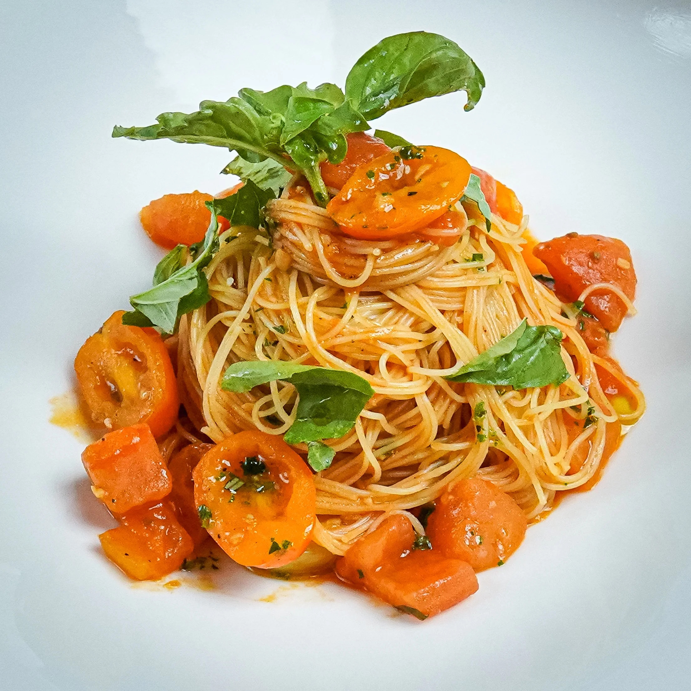 Plate of spaghetti with cherry tomatoes, basil leaves, and pieces of cooked carrots.
