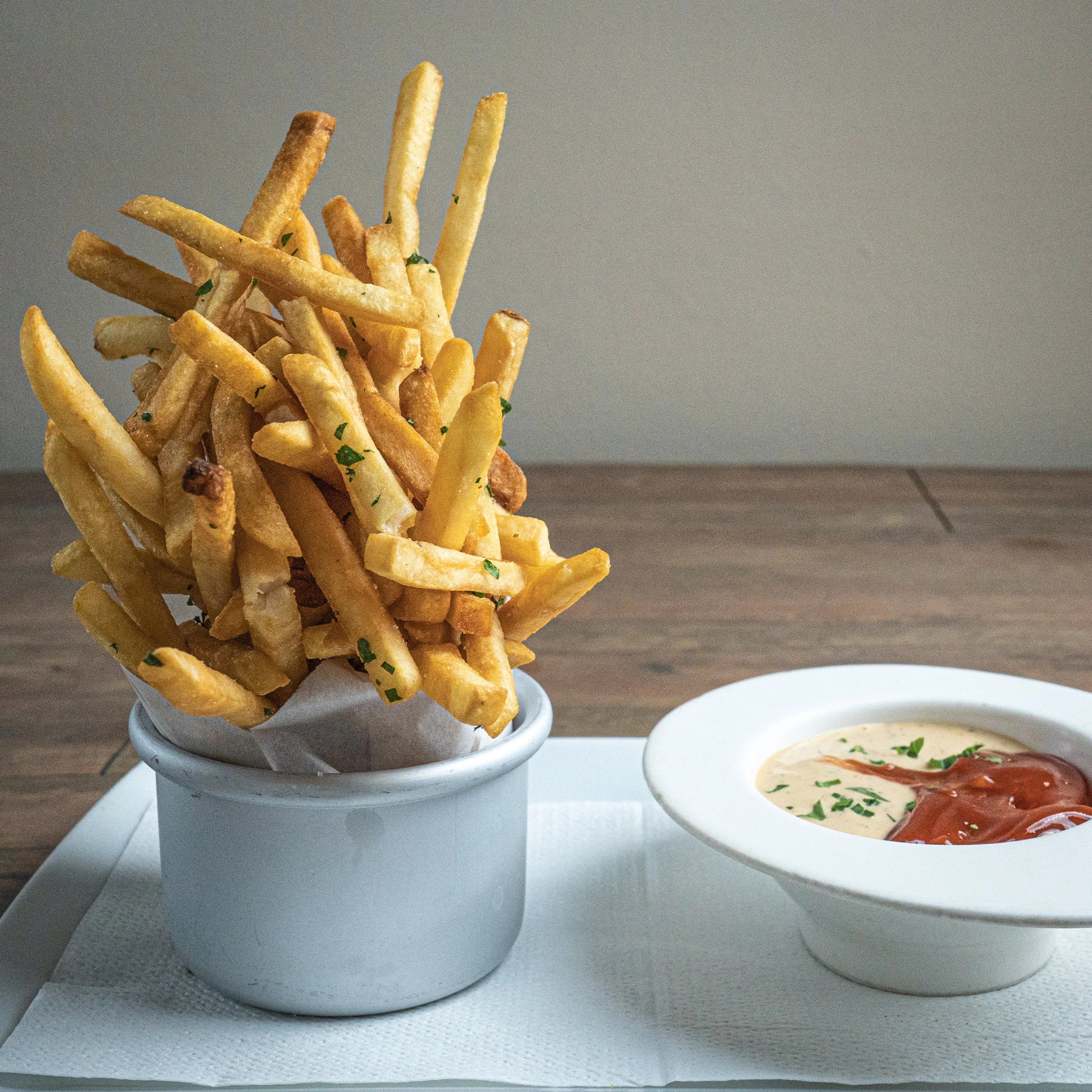 A serving of French fries topped with chopped herbs next to a bowl of cheese sauce with diced tomatoes and herbs on top.