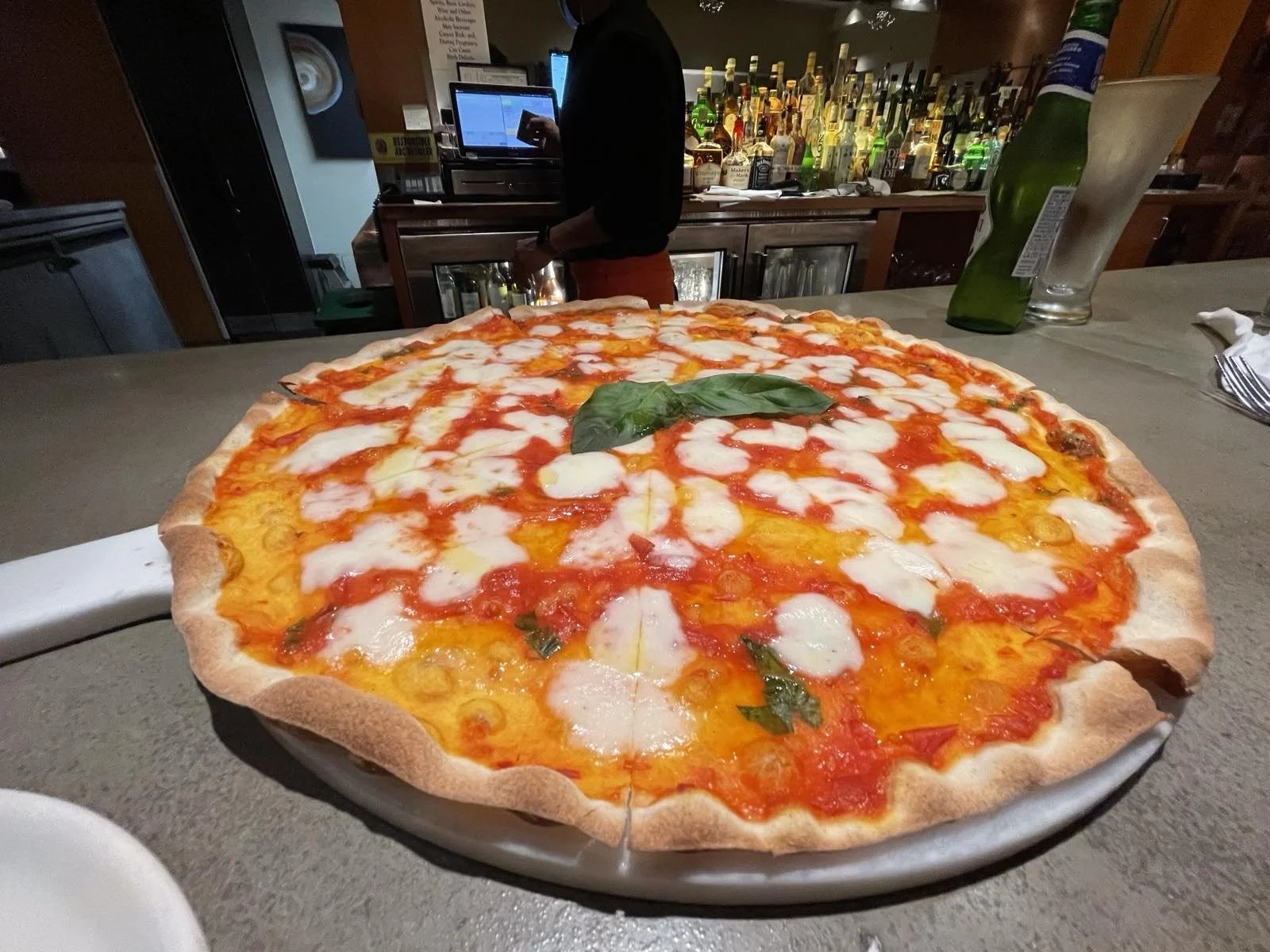 A cheese pizza with a basil leaf on top, on a white plate at a restaurant.