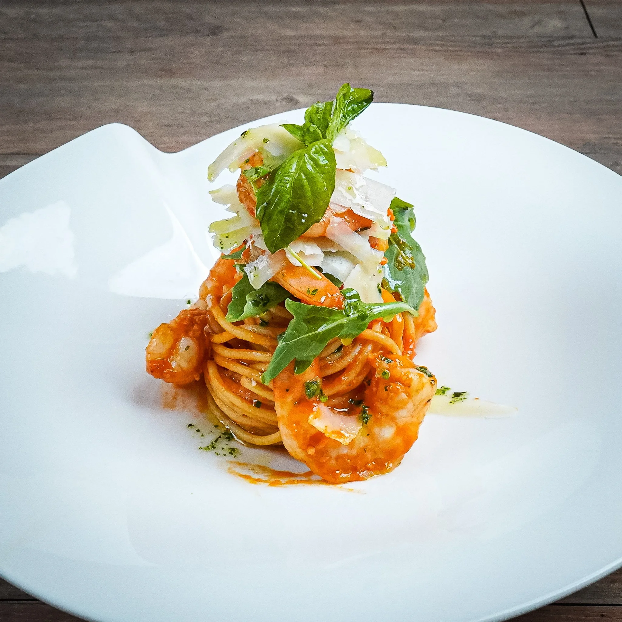 Pasta with shrimp, topped with fresh basil and mixed greens on a white plate.