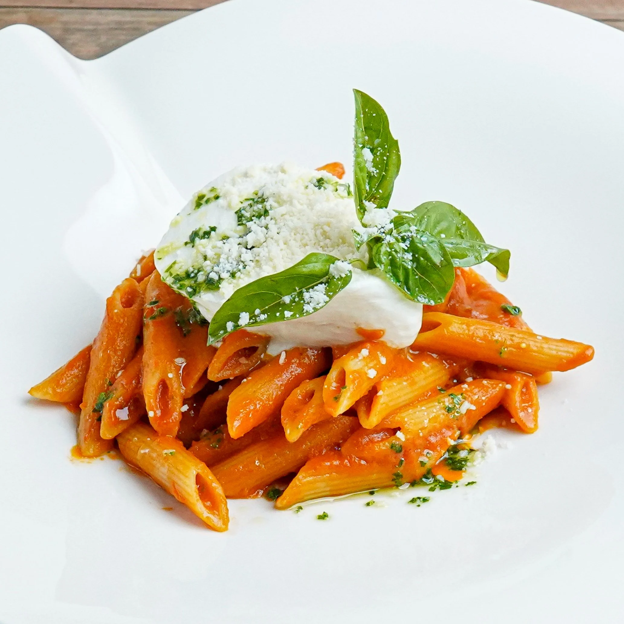 Plate of penne pasta with tomato sauce, topped with basil leaves, shredded cheese, and a dollop of cream or cheese.