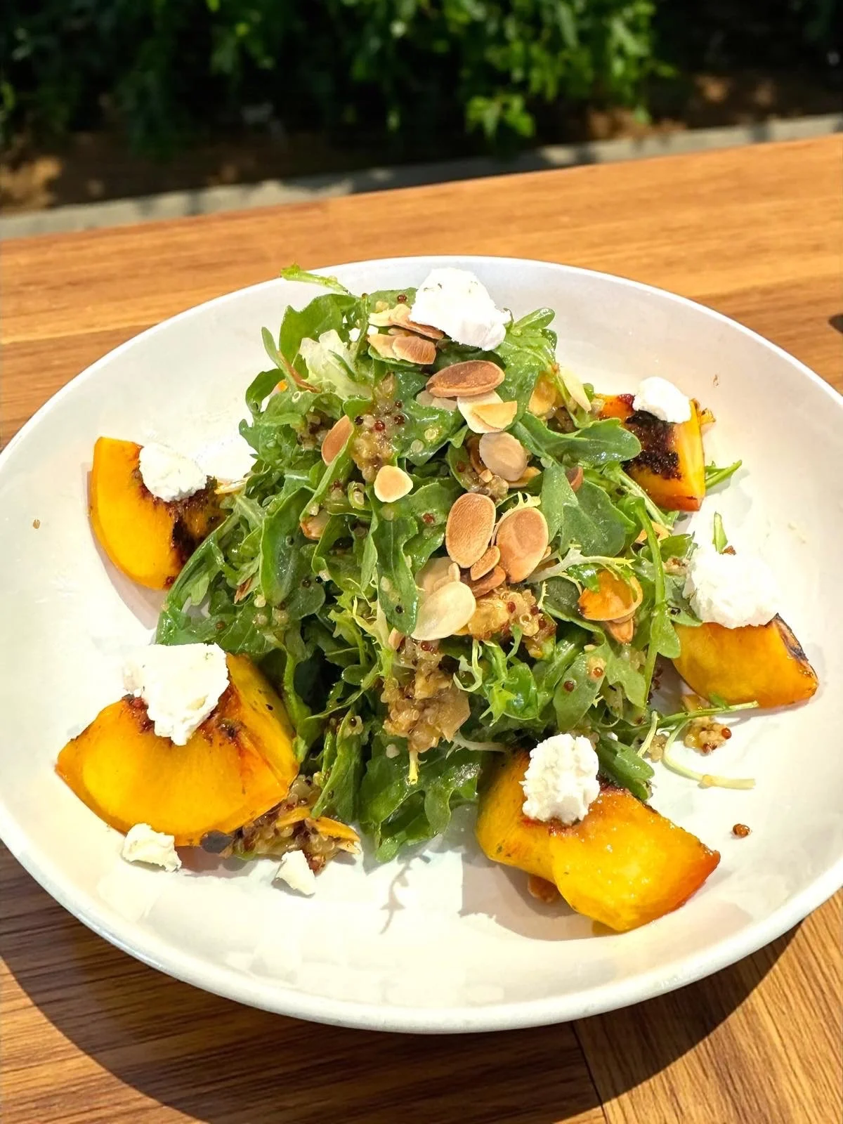 Salad with grilled pumpkin, arugula, goat cheese dollops, and toasted almonds on a white plate.