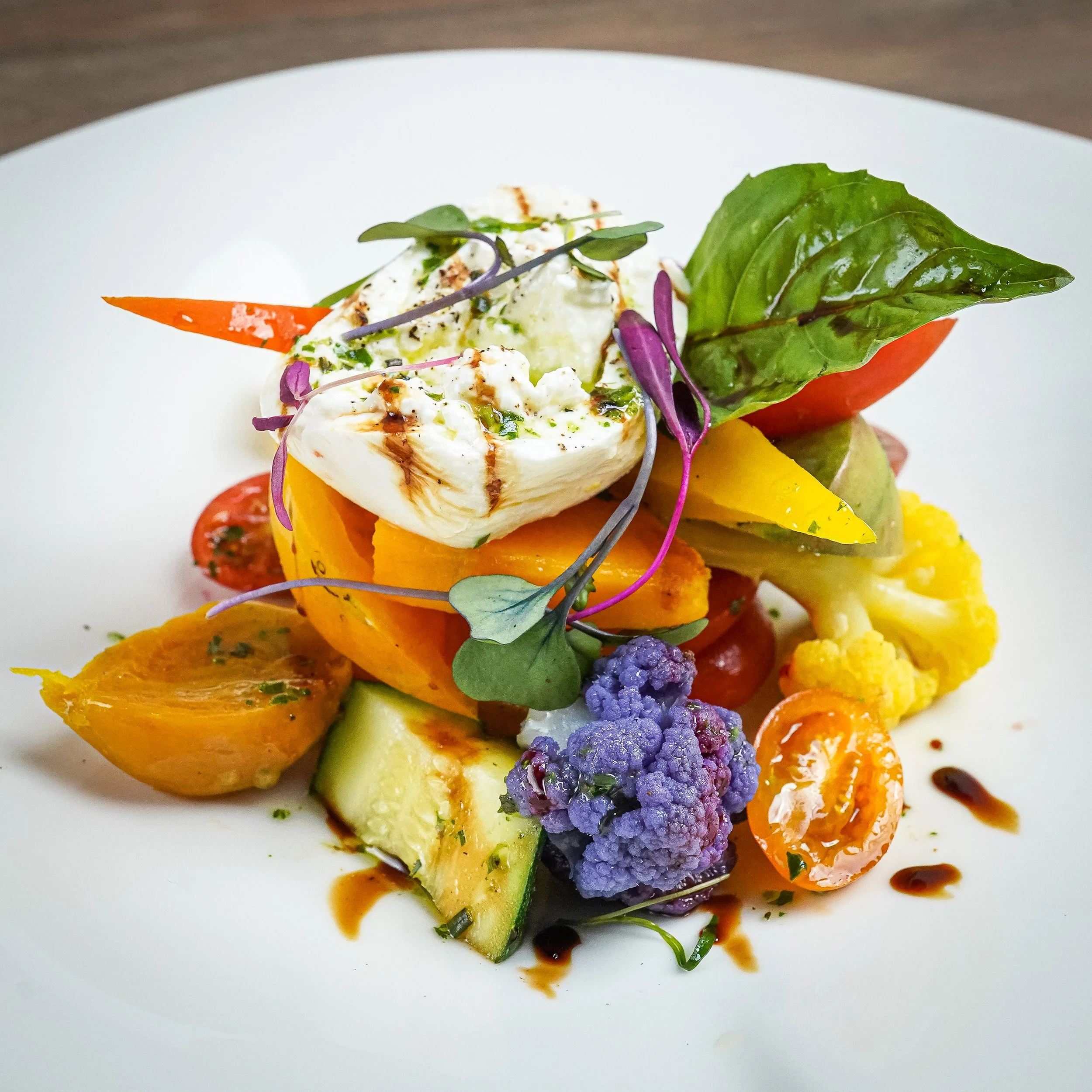 Colorful grilled vegetable salad with mozzarella, cherry tomatoes, cauliflower, cucumber, and fresh basil on a white plate.