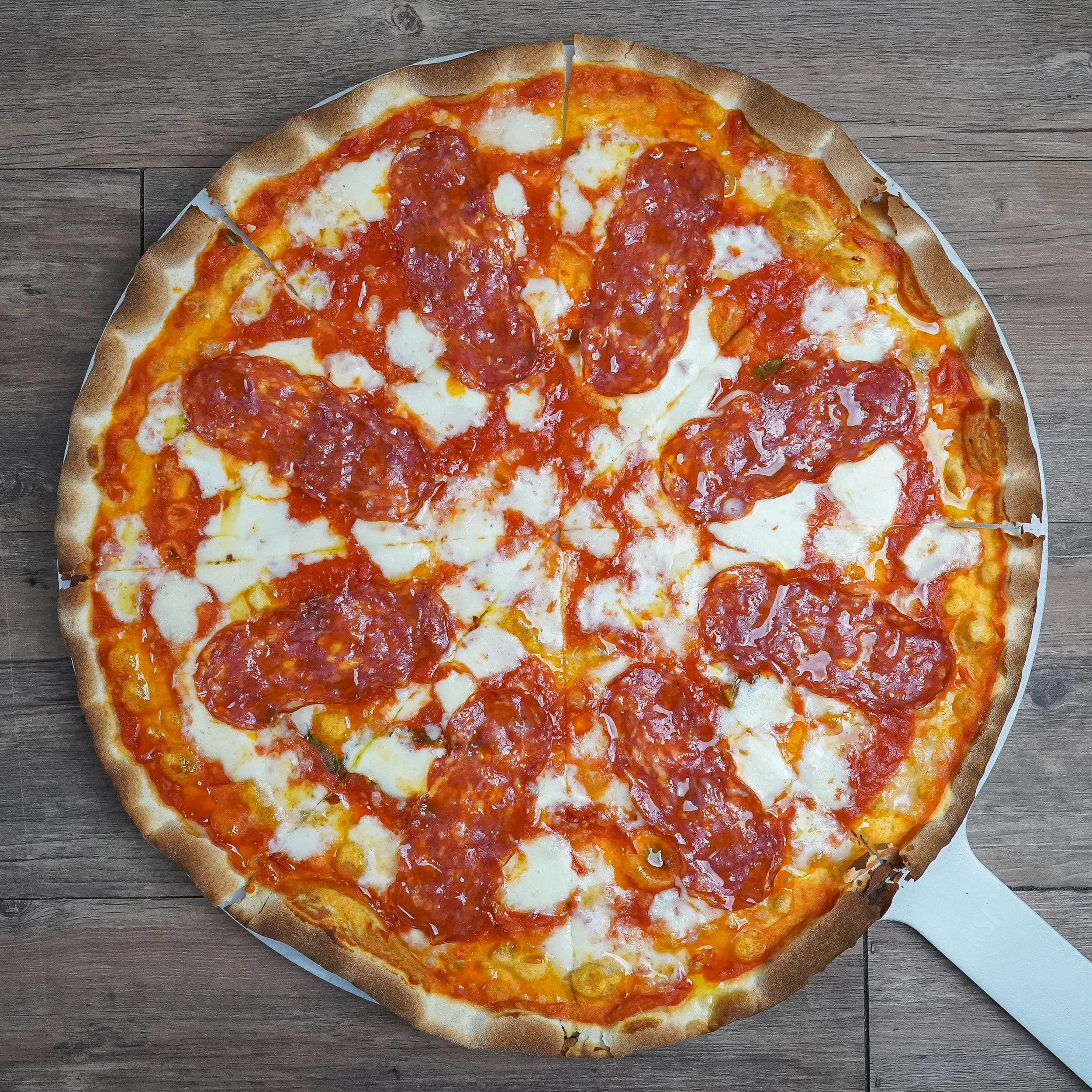 A pepperoni pizza on a round white tray with a wooden surface background.