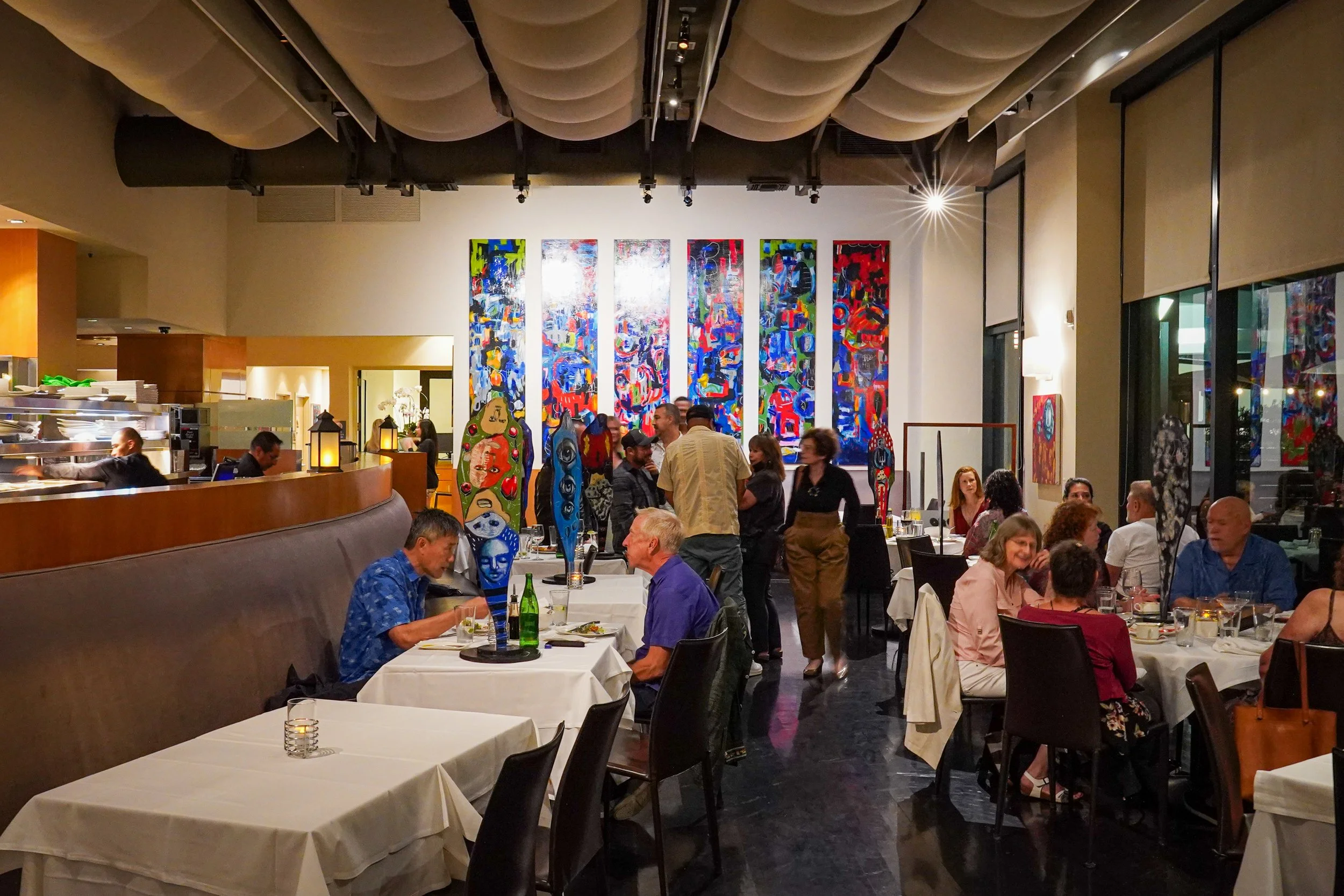 Interior of a lively restaurant with white tablecloths, various artworks on the walls, and several diners enjoying their meals.
