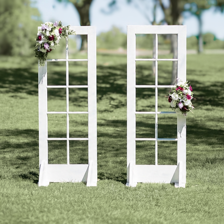 Two white window frame decorations with flower arrangements, set outdoors on grass, likely for a wedding or event backdrop.