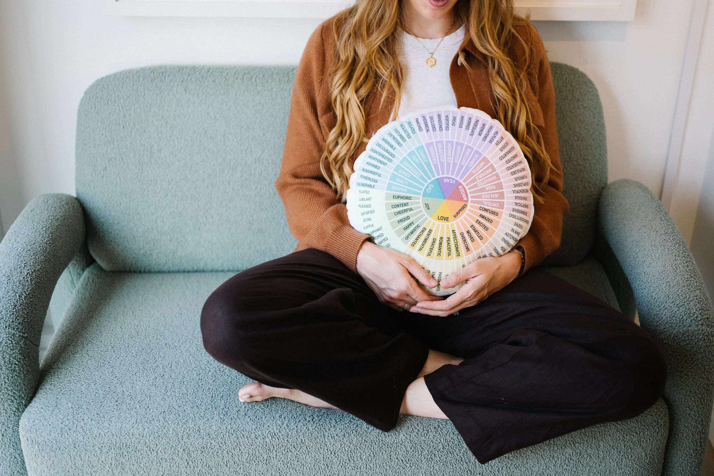 Person sitting cross-legged on a green sofa holding a circular color chart with words related to emotions and feelings.
