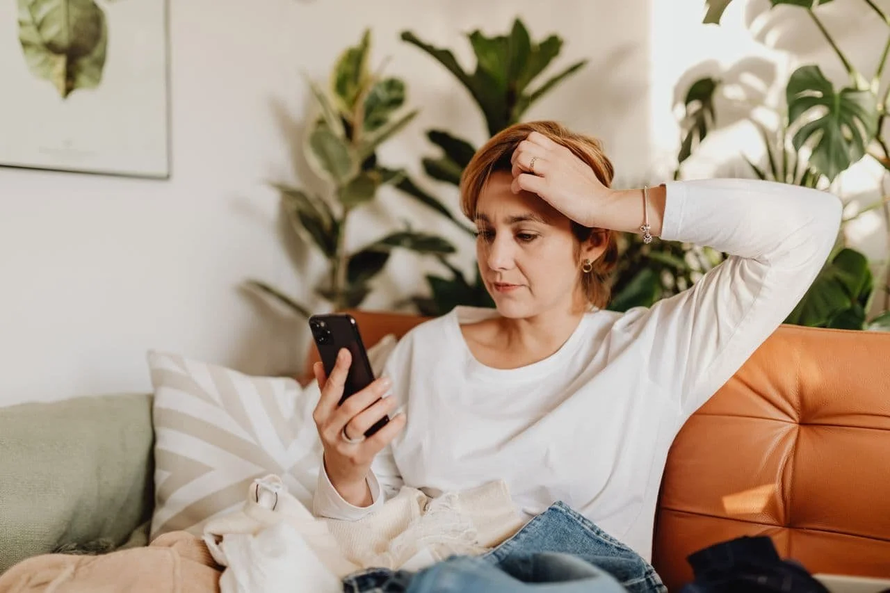 woman-sitting-on-sofa-looking-at-phone-and-scratching-her-head