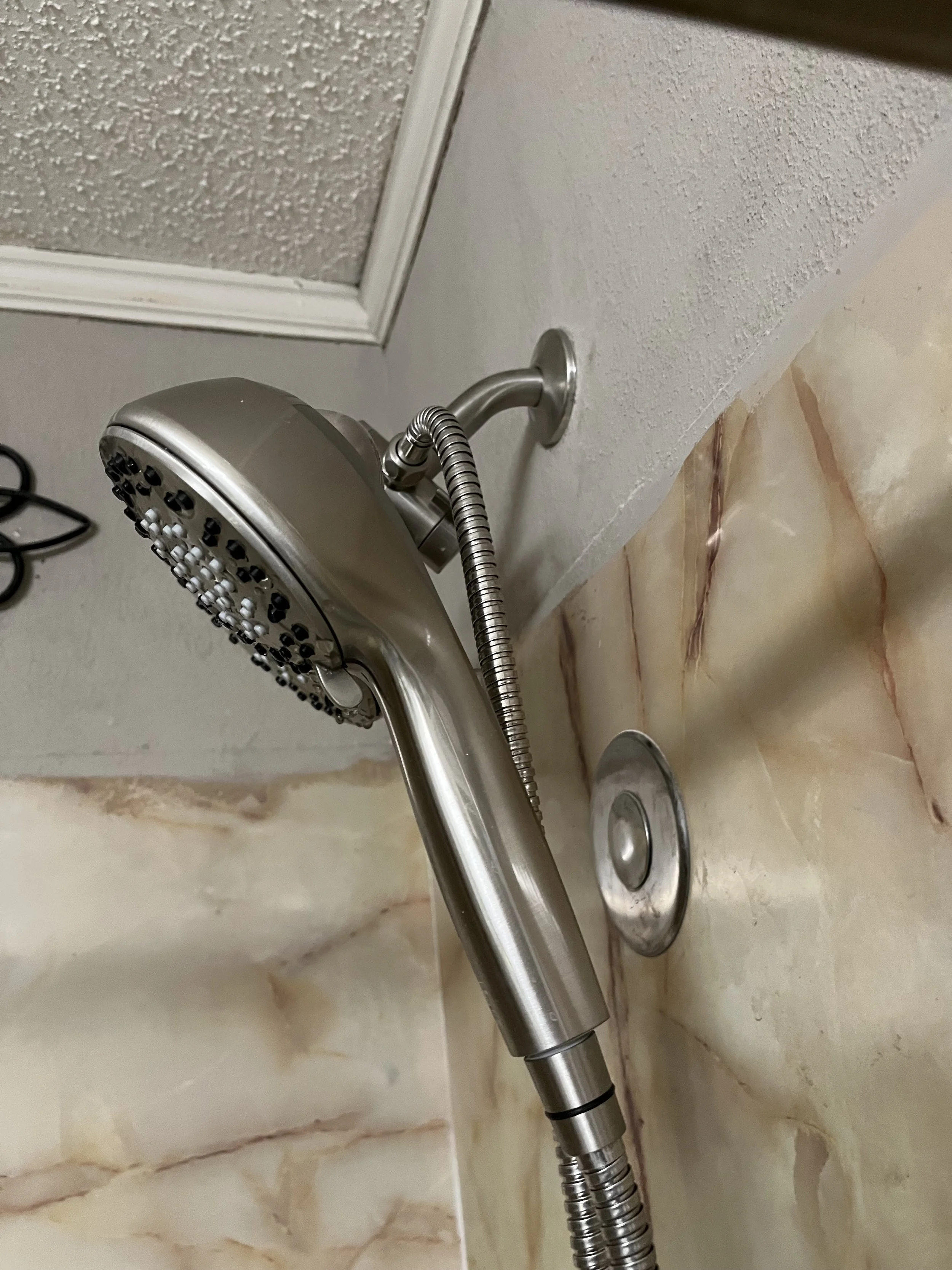 Close-up of a metal handheld showerhead mounted on a tiled wall in a bathroom.