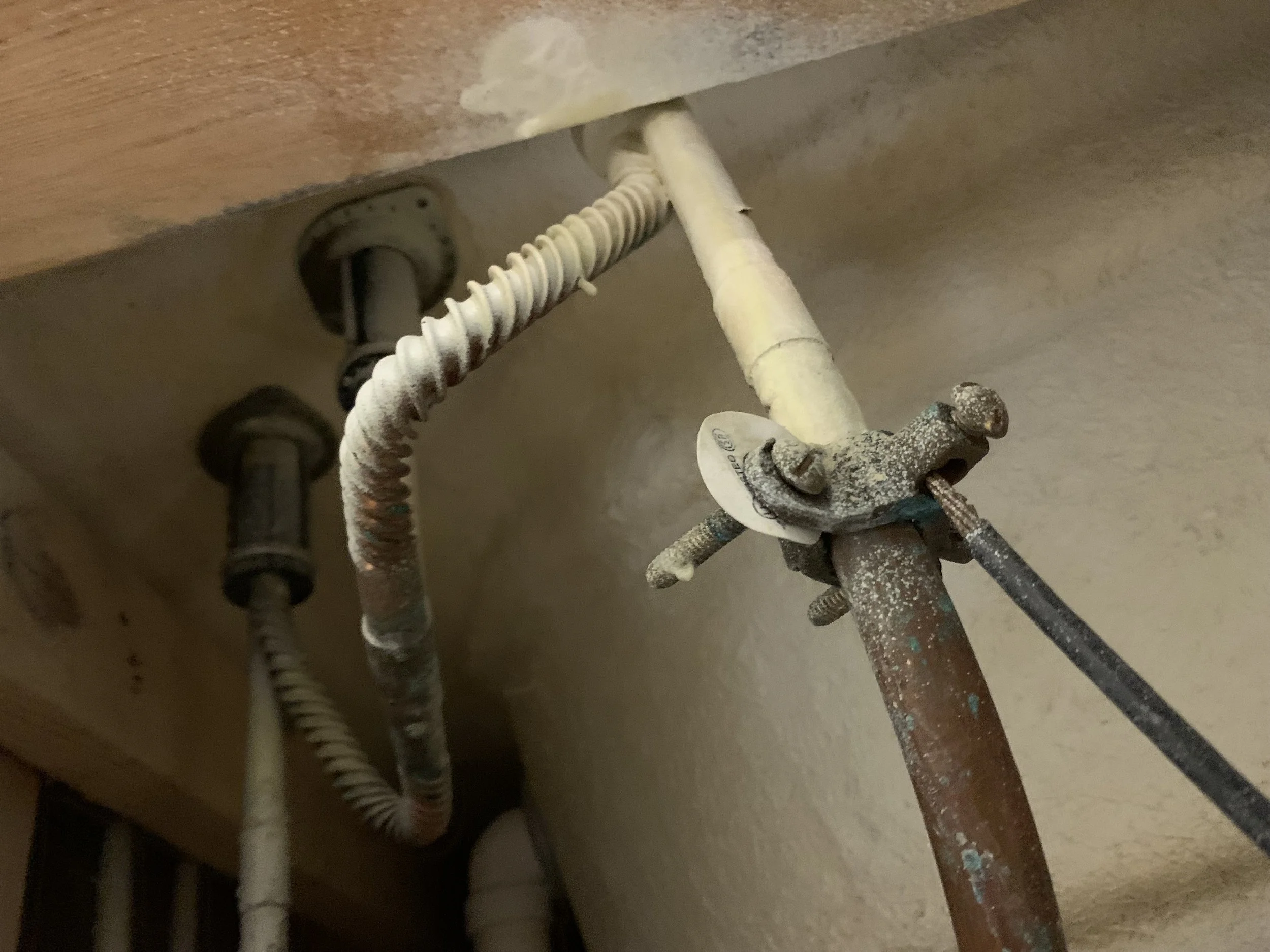 Close-up of rusted and dusty plumbing pipes and fittings under a kitchen sink.