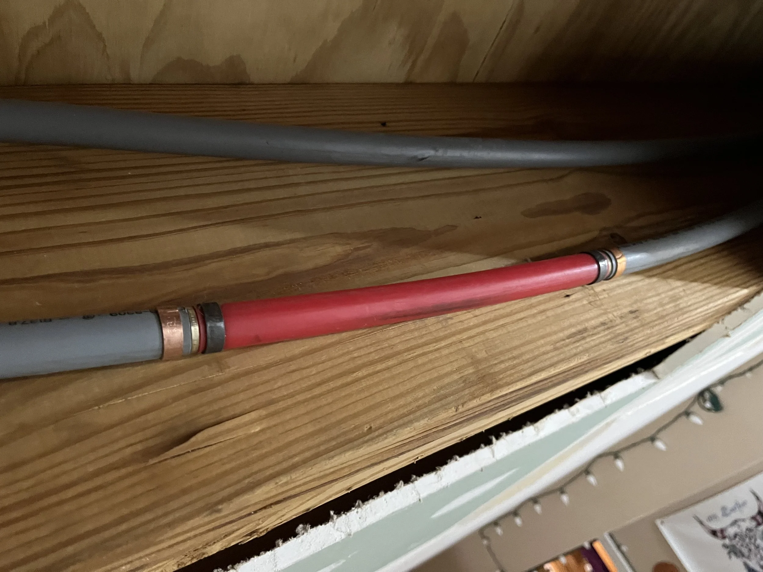 Electrical wires running through a wooden space, with one wire colored red and the others gray, connected by copper fittings.