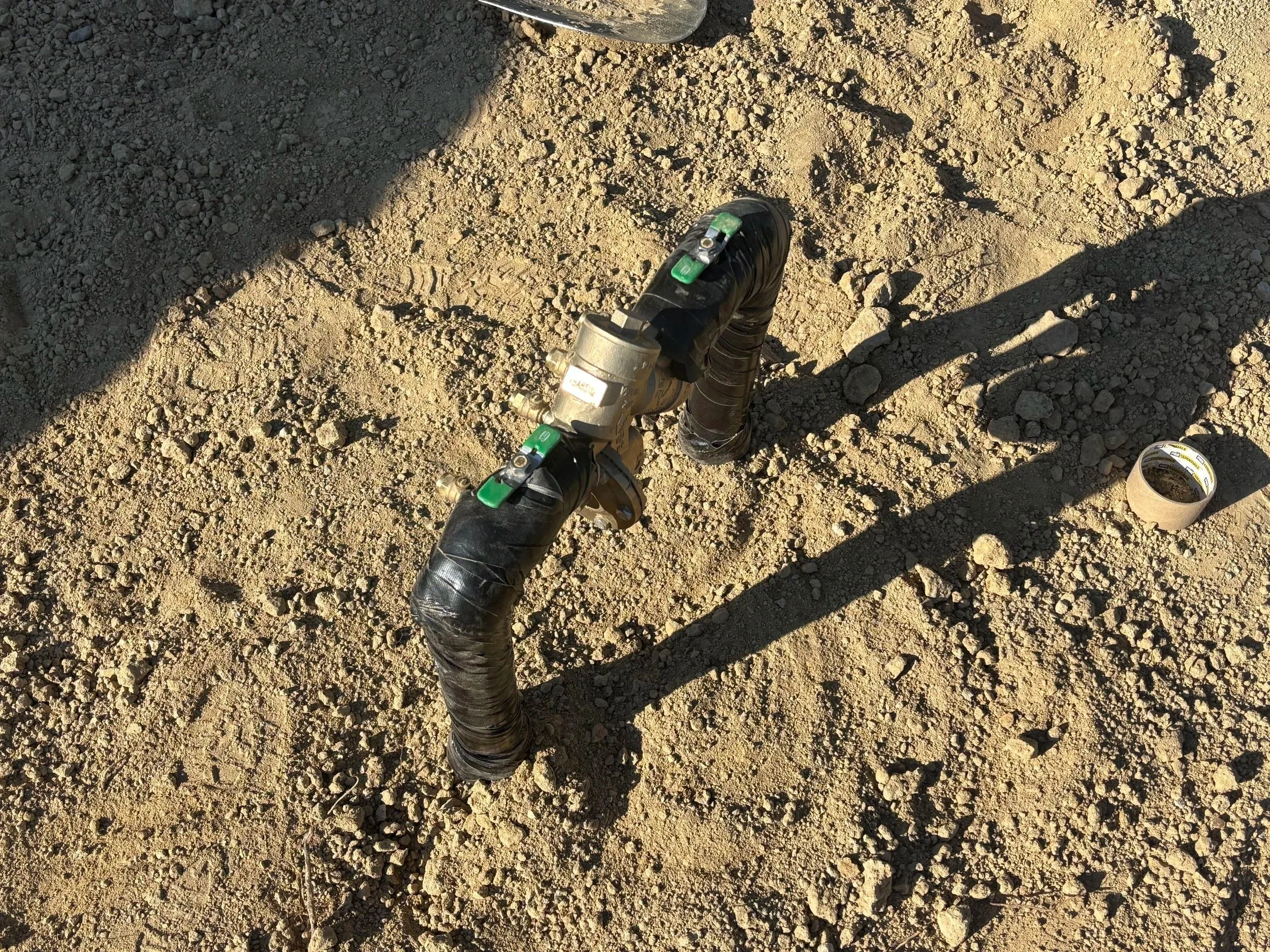 A modified pipeline with black insulation tape on the ground, with shadow and a roll of tape nearby.