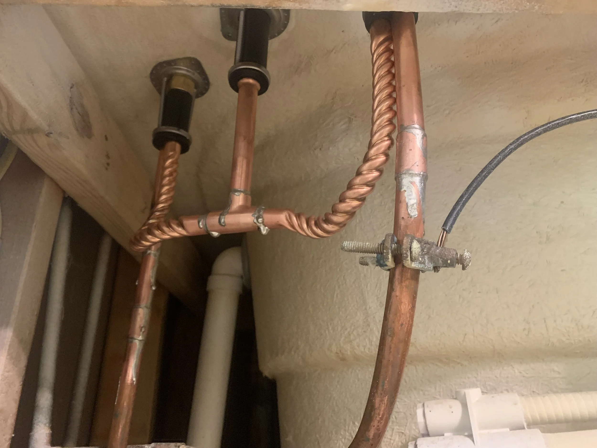 Close-up of copper water pipes with fittings and insulation, attached to a wall and ceiling.