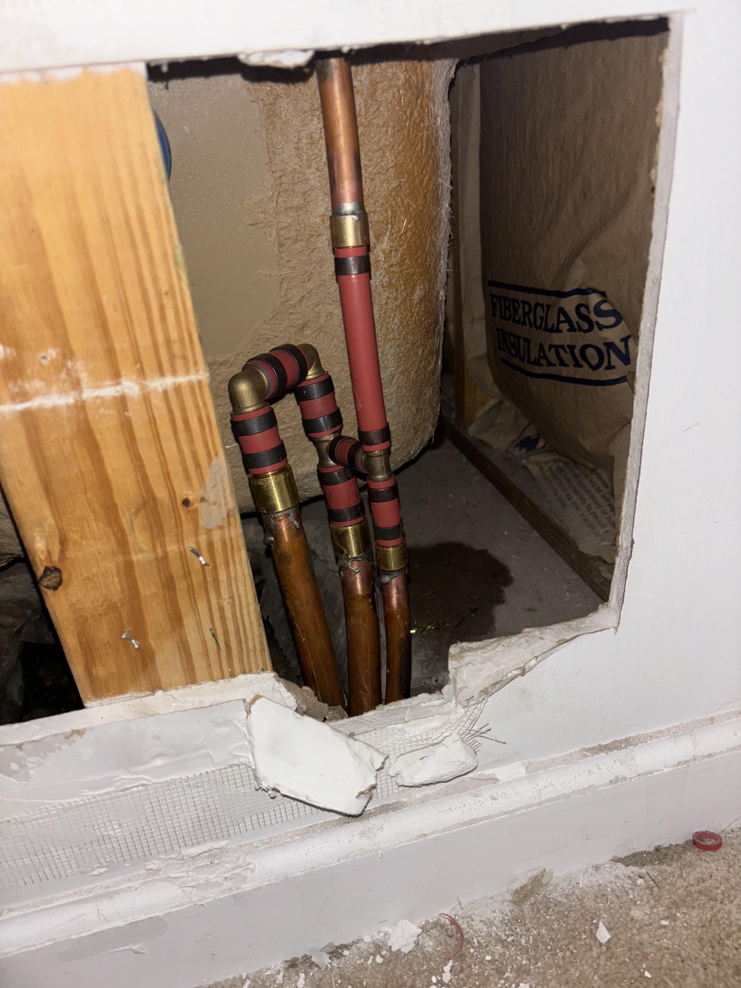 Plumbing pipes with copper and PEX, insulation, and a hole in the wall in a construction or renovation setting.