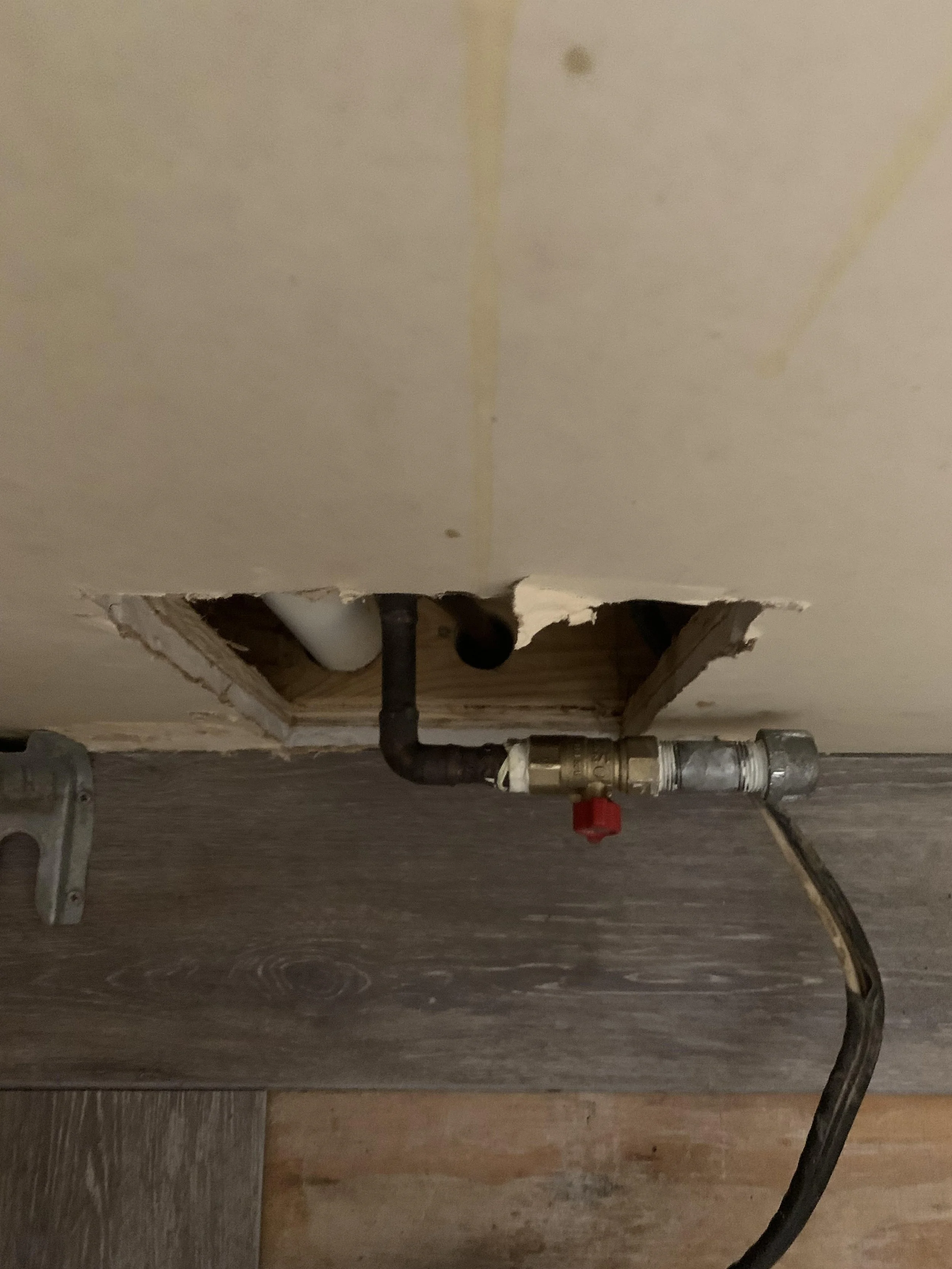 View of plumbing pipes and valves through a cutout in a drywall ceiling with exposed wooden framing, and a plastic pipe.