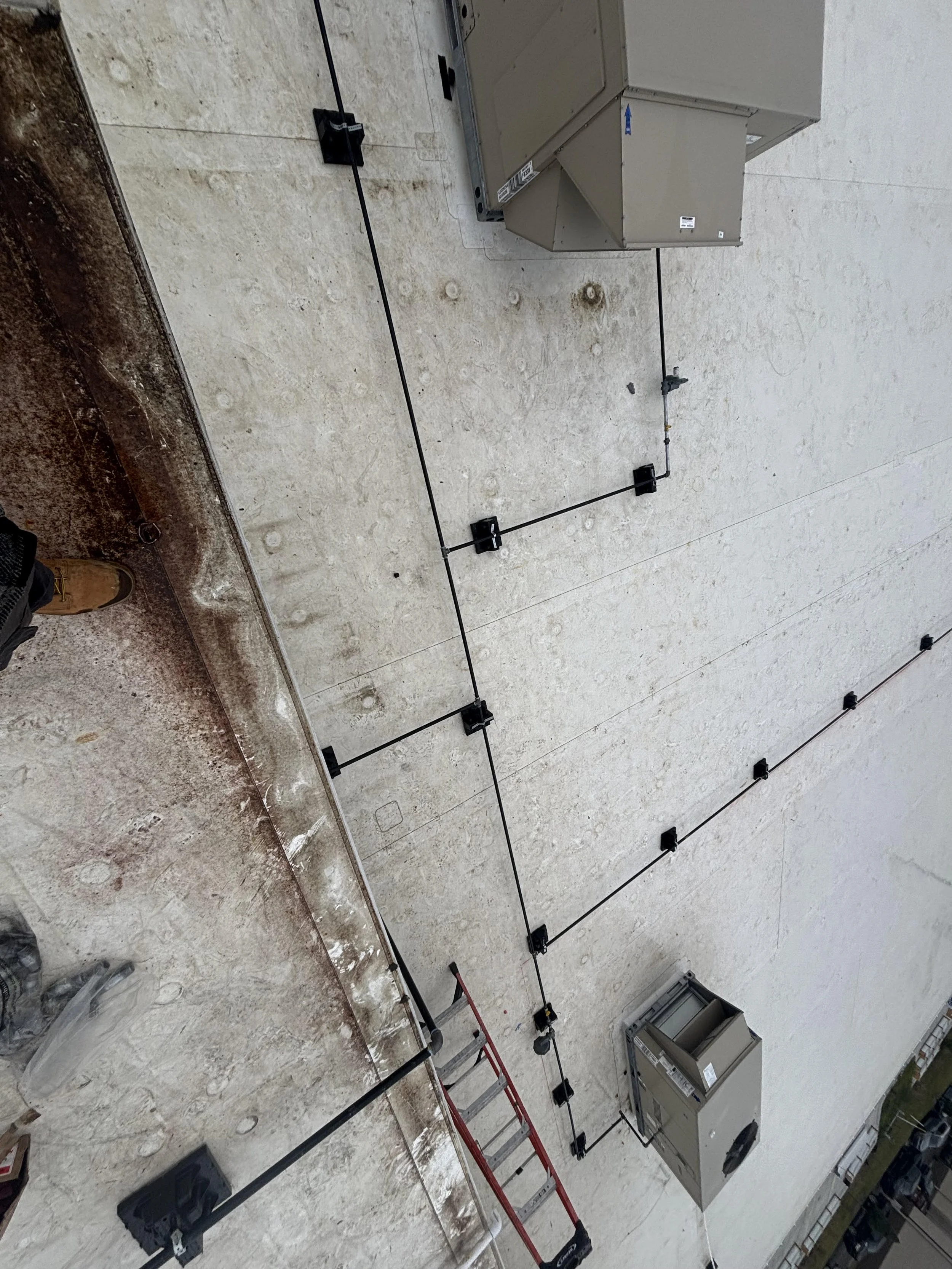 Electrical conduit wires attached to a wall on an outdoor building, with electrical boxes, HVAC units, ladders, and construction tools visible.