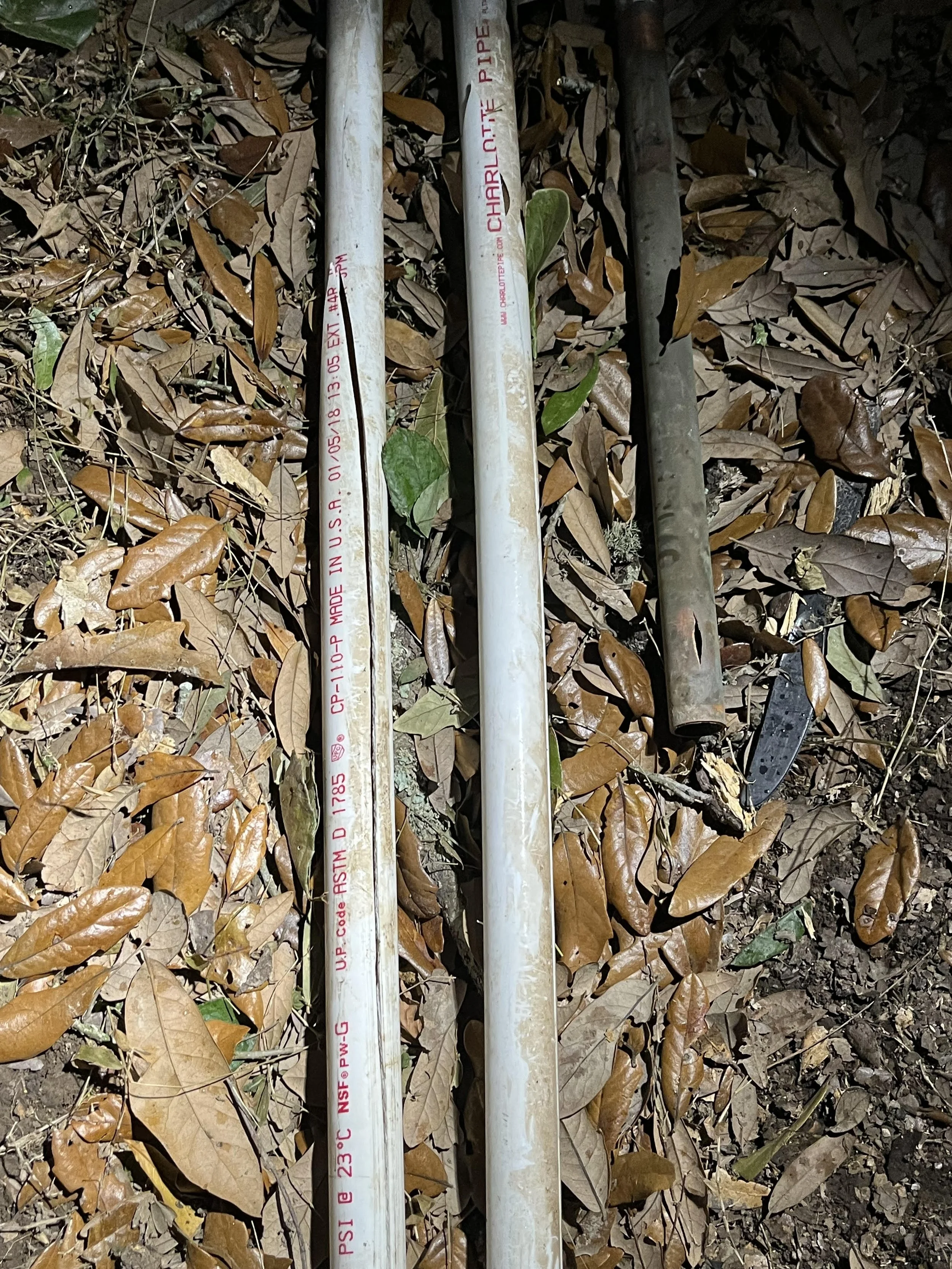 Three metal pipes lying on the ground covered with dry leaves and twigs.