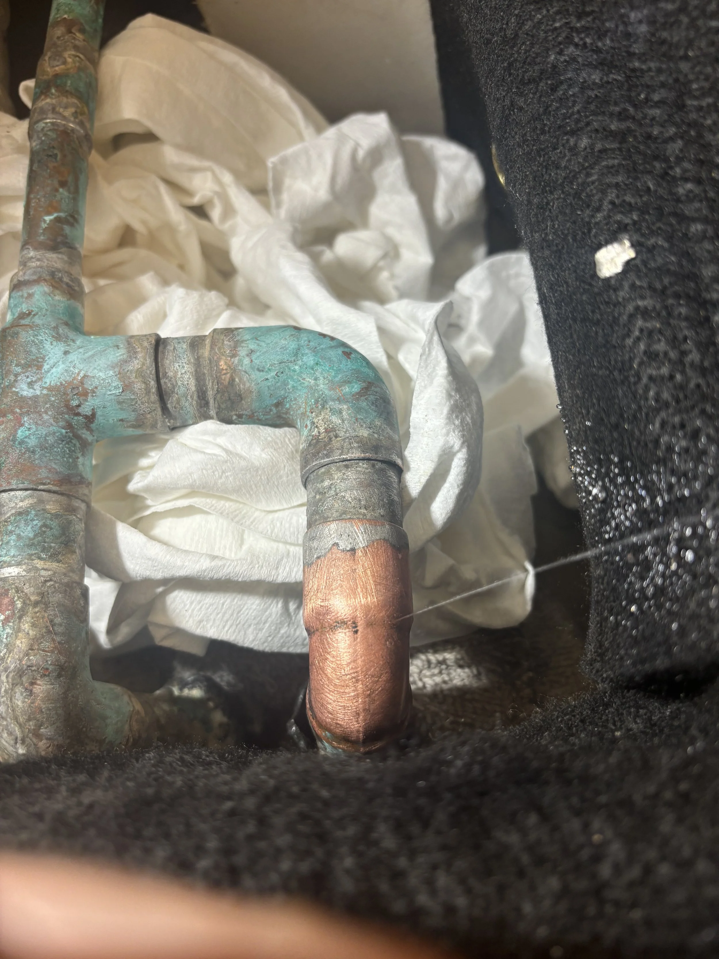 Close-up of corroded copper and steel pipes on a black surface with crumpled white tissues underneath.