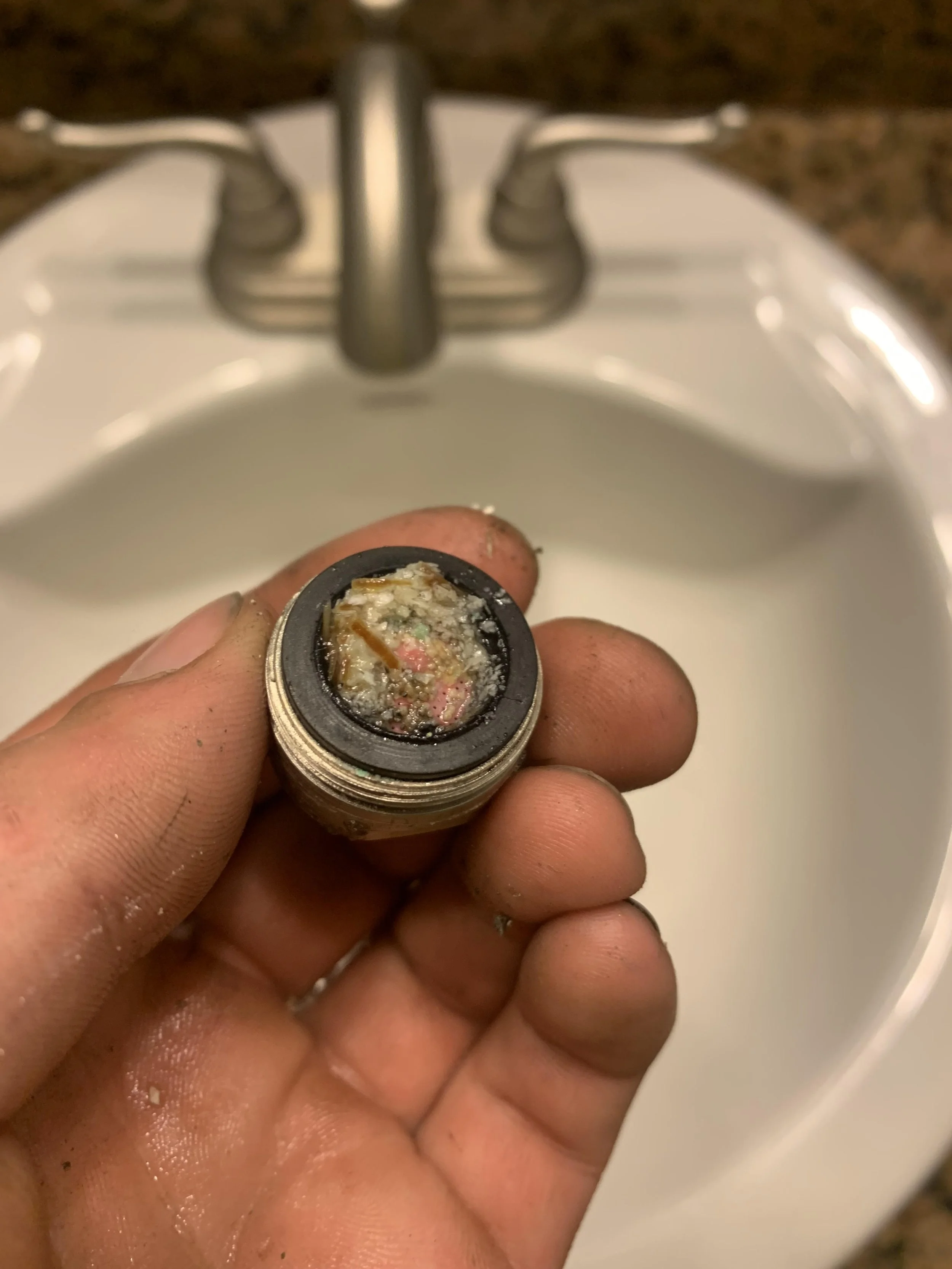 Close-up of a dirty hand holding a small metal container filled with blackened, tarnished, and burnt residue over a sink with a faucet.