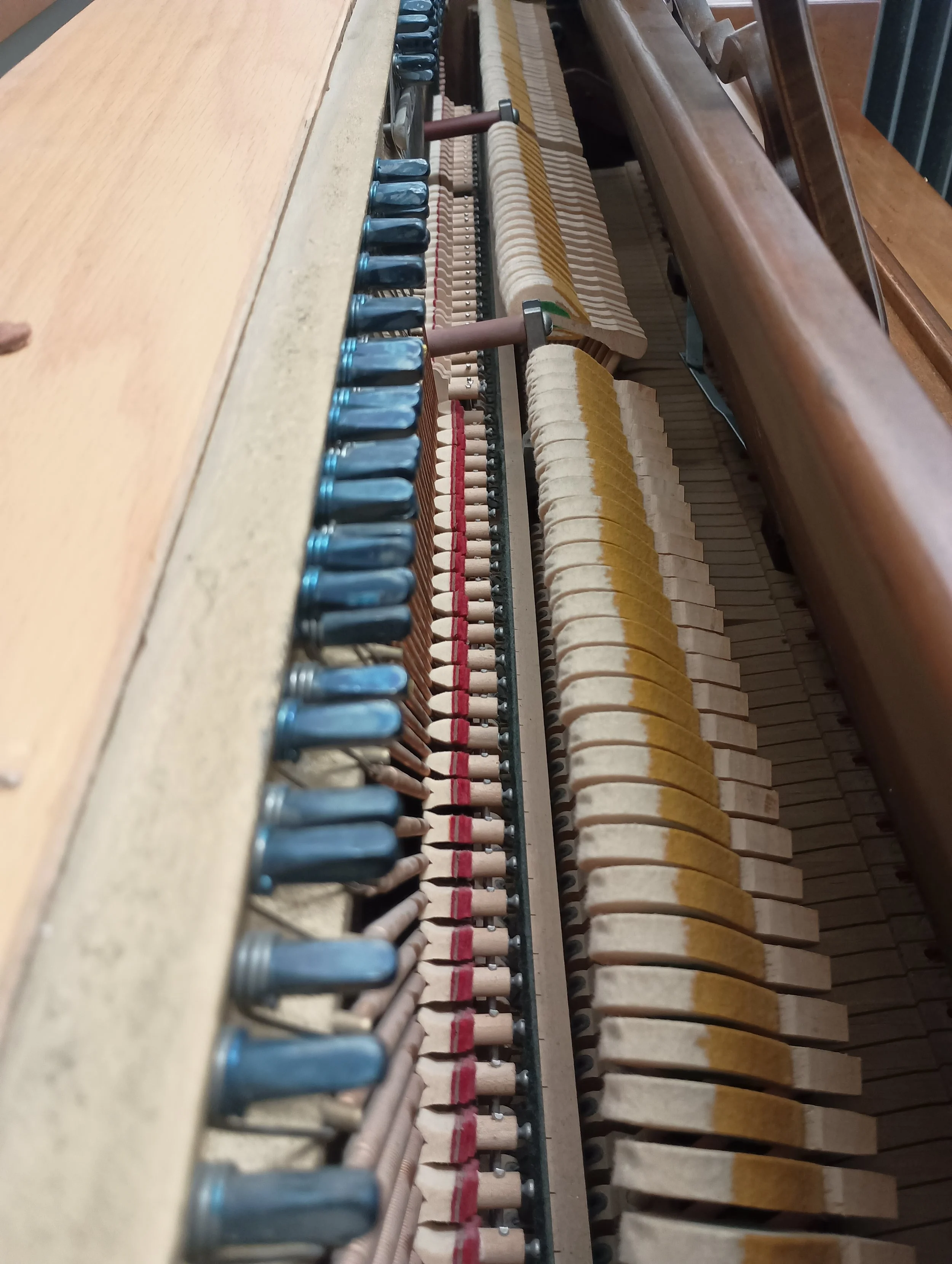 Inside view of an upright piano, showing tuning pins, hammers, dampers, and strings.