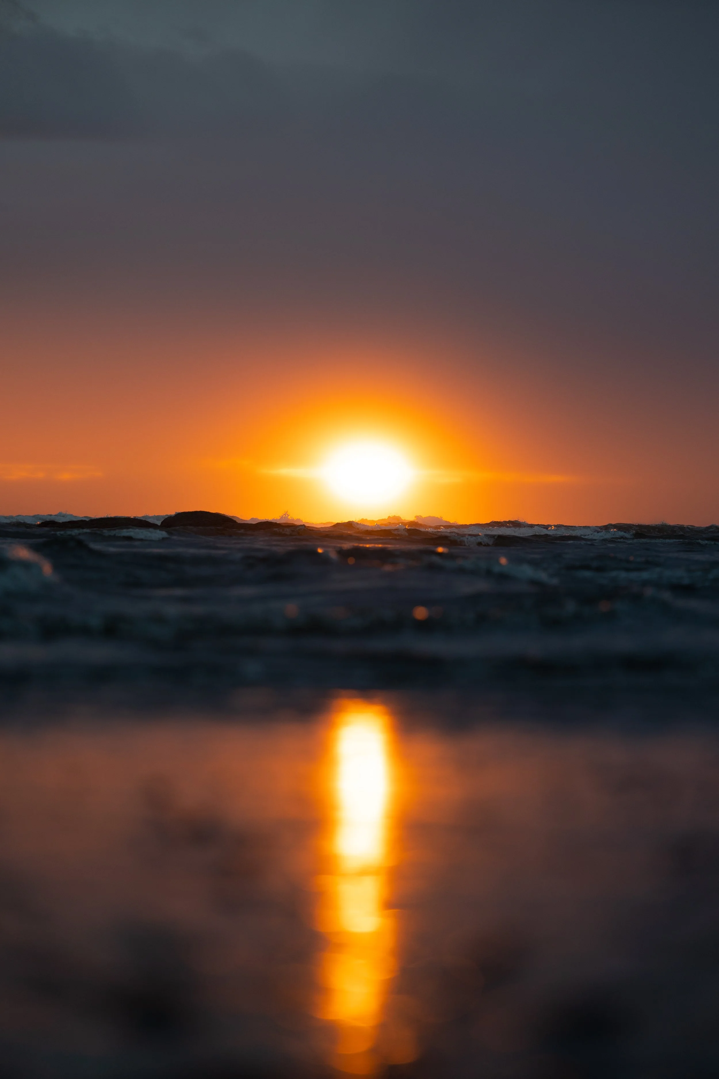 Sunset over the ocean with waves and a reflection of the sun on the water
