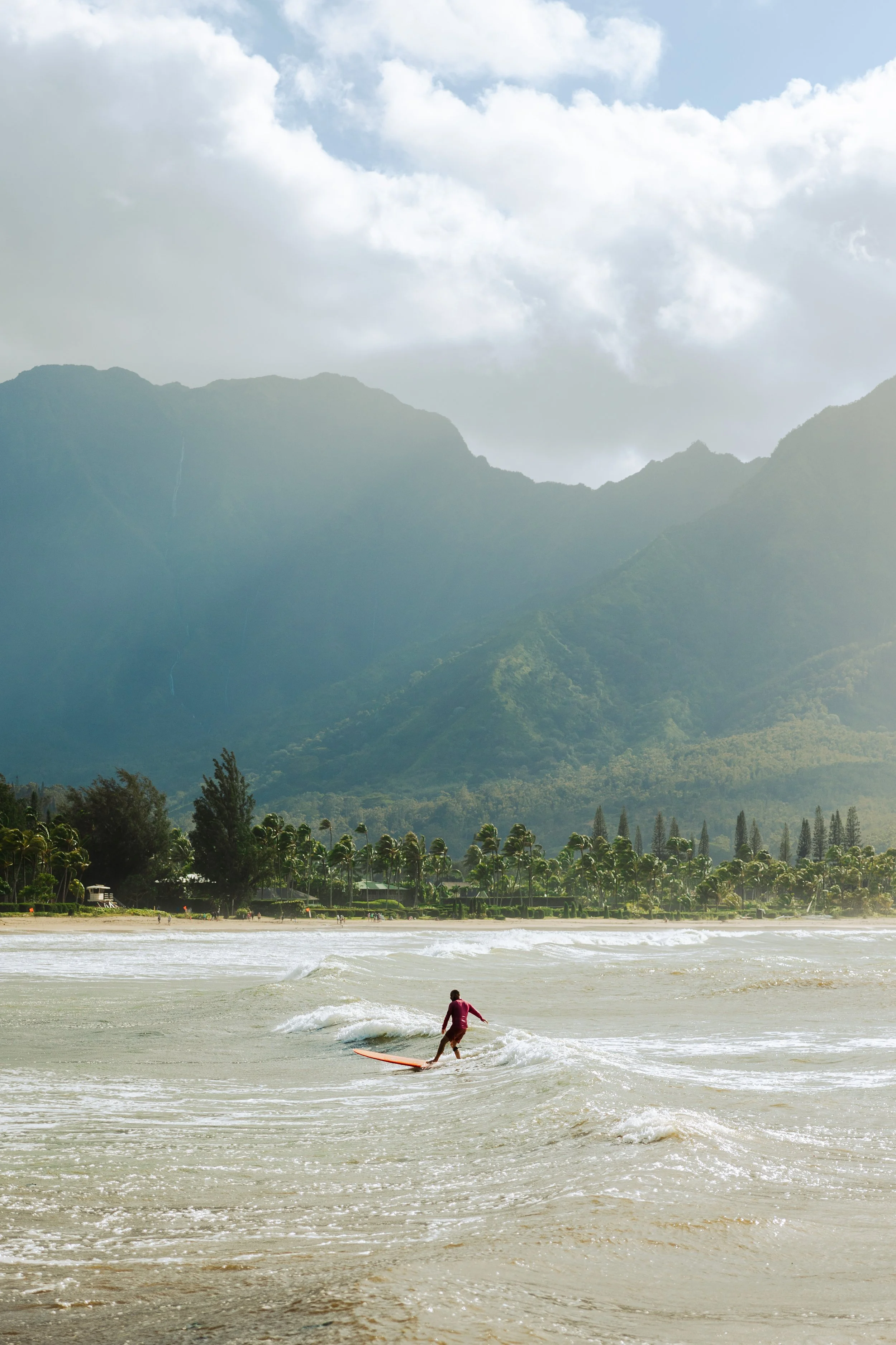 A person surfing on a wave in the ocean with distant mountains and a cloudy sky in the background.