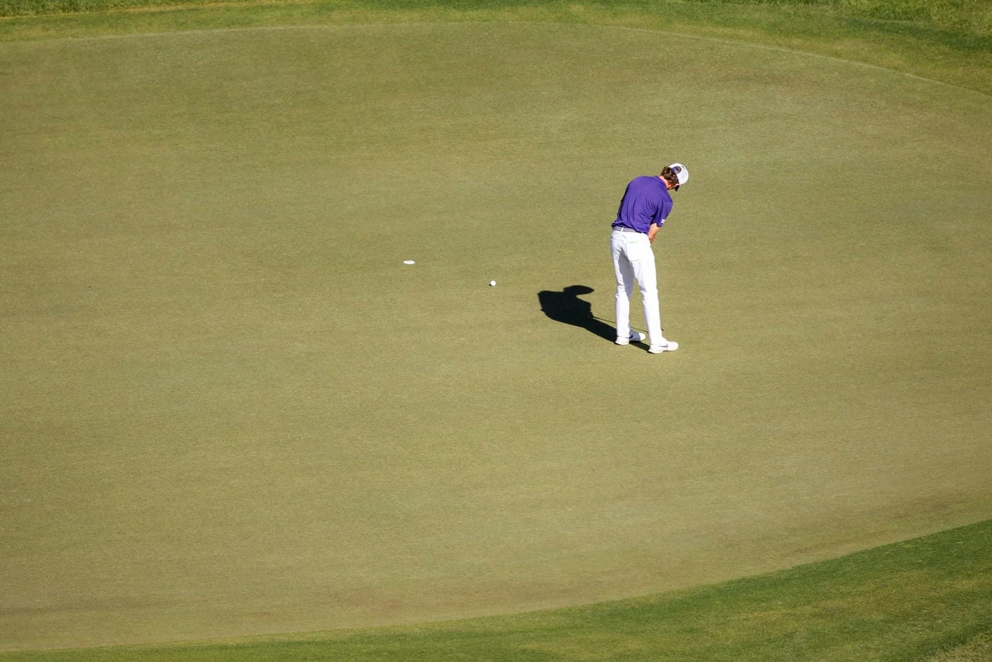 A golfer stands on the green, preparing to putt a golf ball