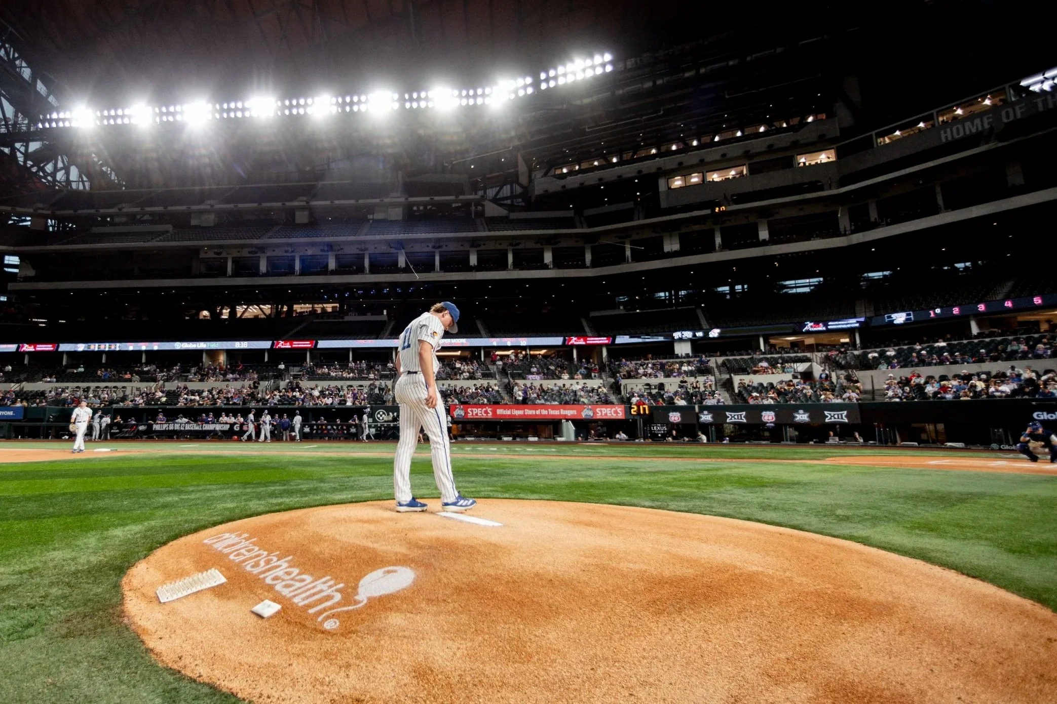 A baseball pitcher in a stadium preparing to pitch, with spectators in the stands and the playing field visible.