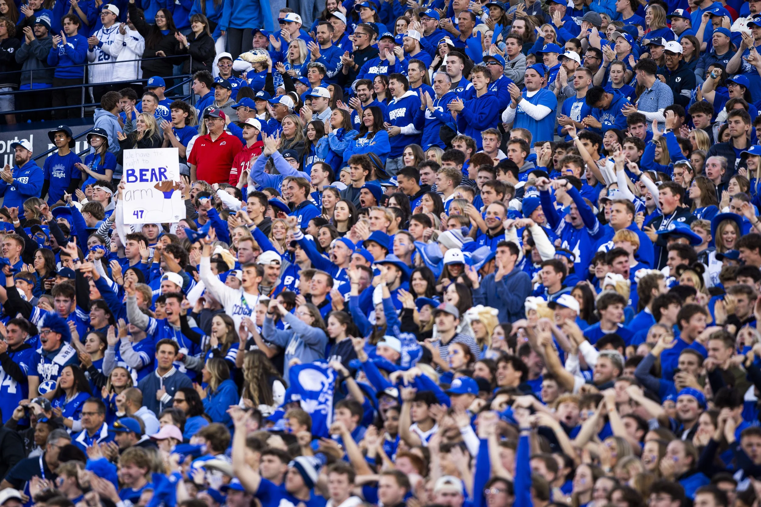 A large crowd of sports fans, mostly dressed in blue, cheering and clapping at a stadium.