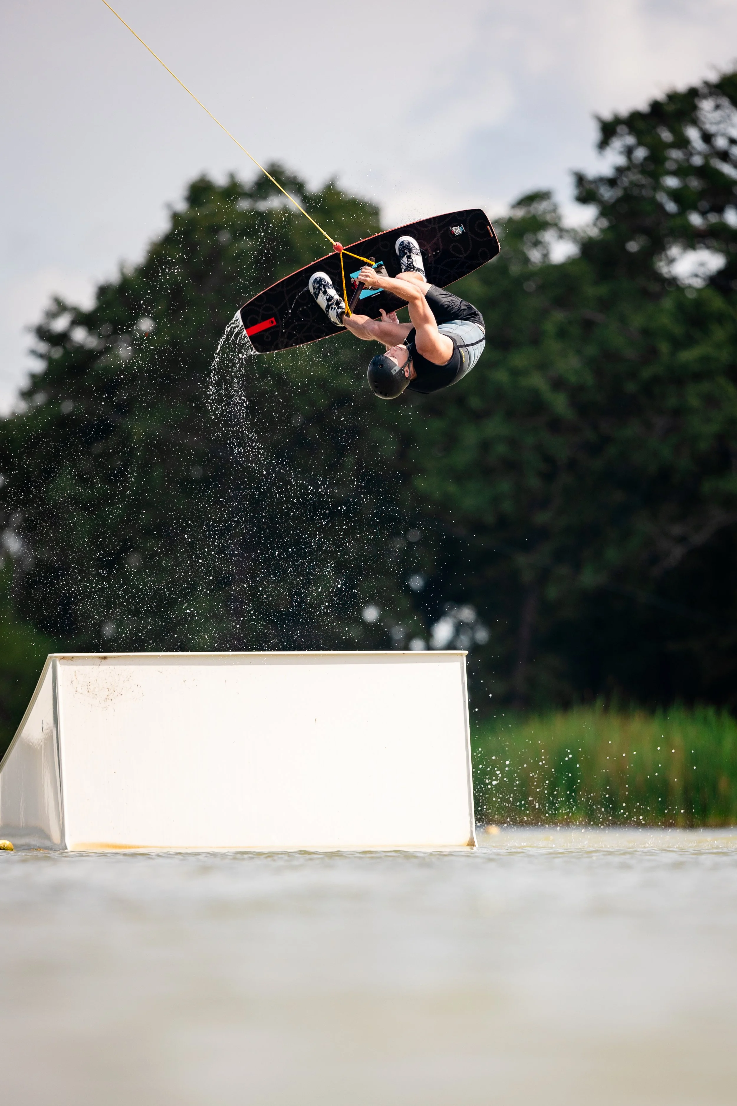 A person wakeskating in the air after launching off a ramp, holding onto a yellow tow rope with a water spray around.