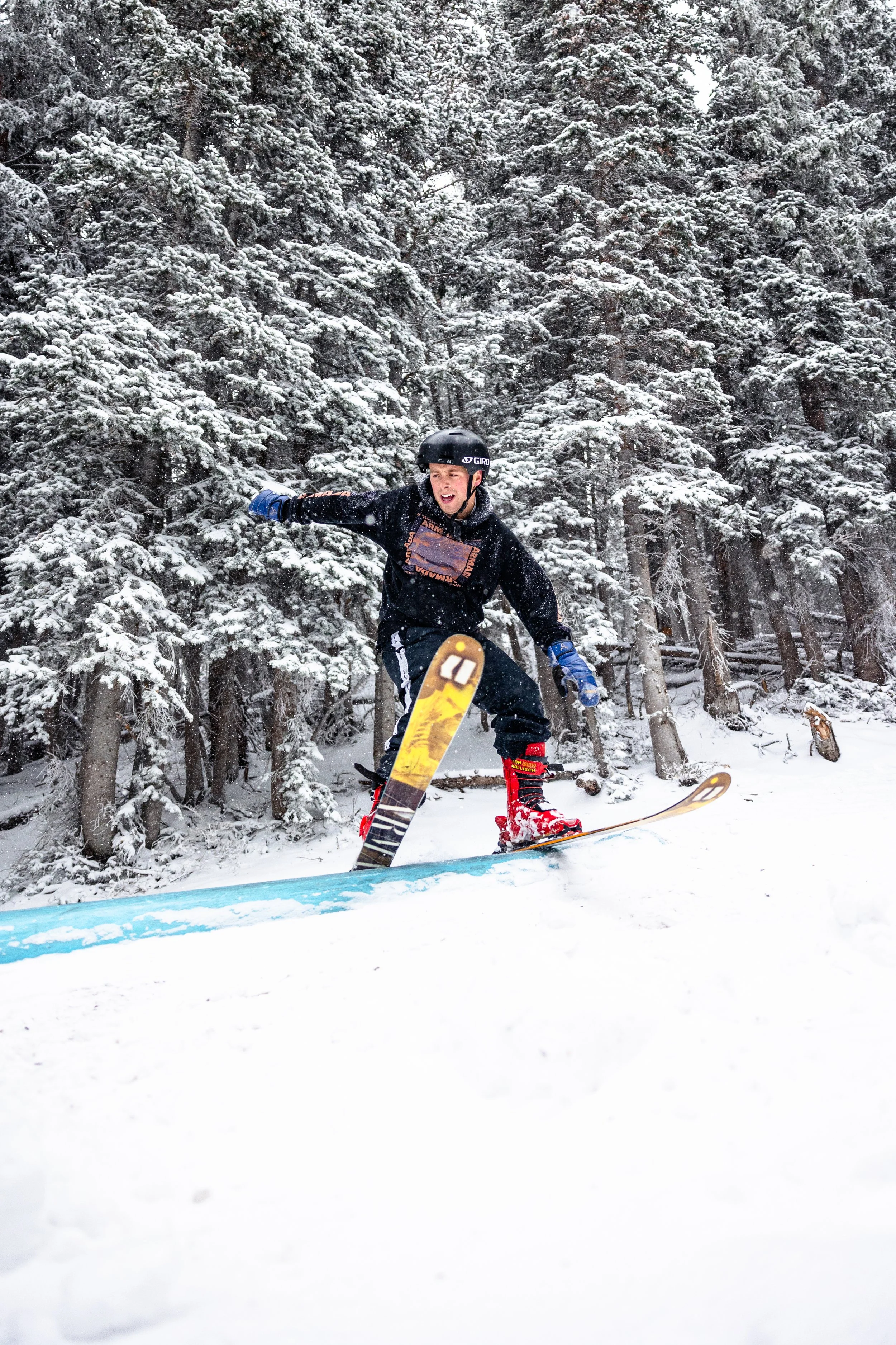 A young boy wearing a helmet, goggles, and winter clothing snowboarding down a snowy slope in a forested area with snow-covered trees.
