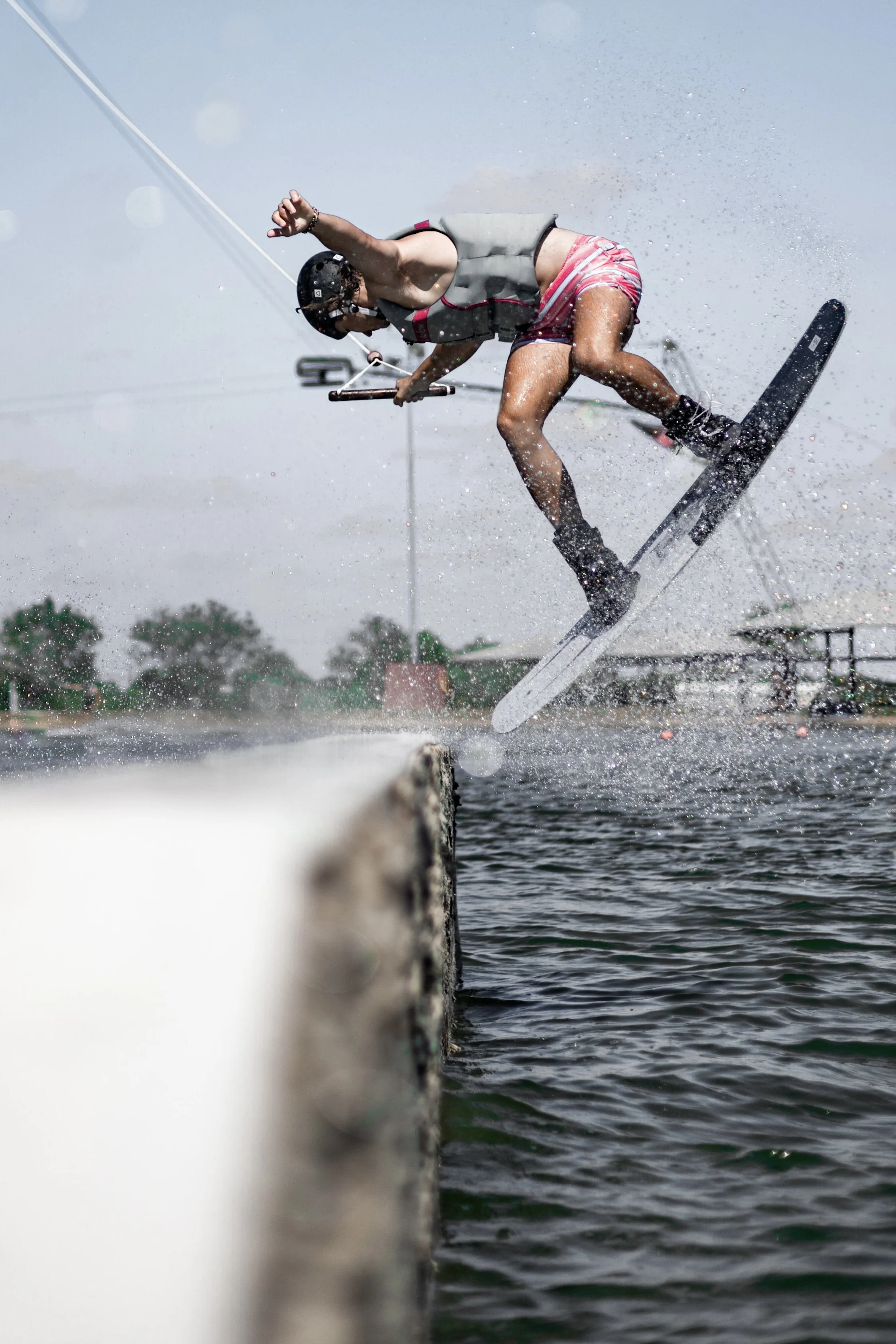 A person wearing a helmet and life jacket performing a jump on wakeboard over water, with water spray and wake behind.