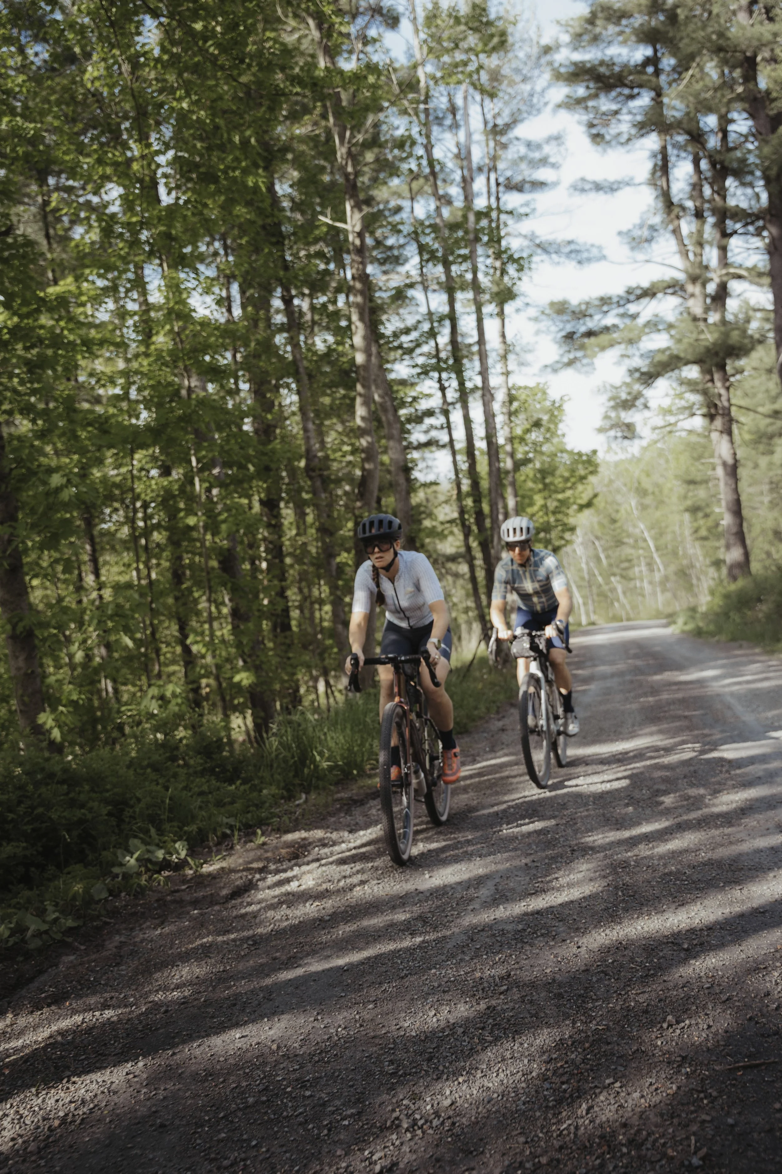 Two women riding mountain bikes on a dirt trail surrounded by trees in a forest.