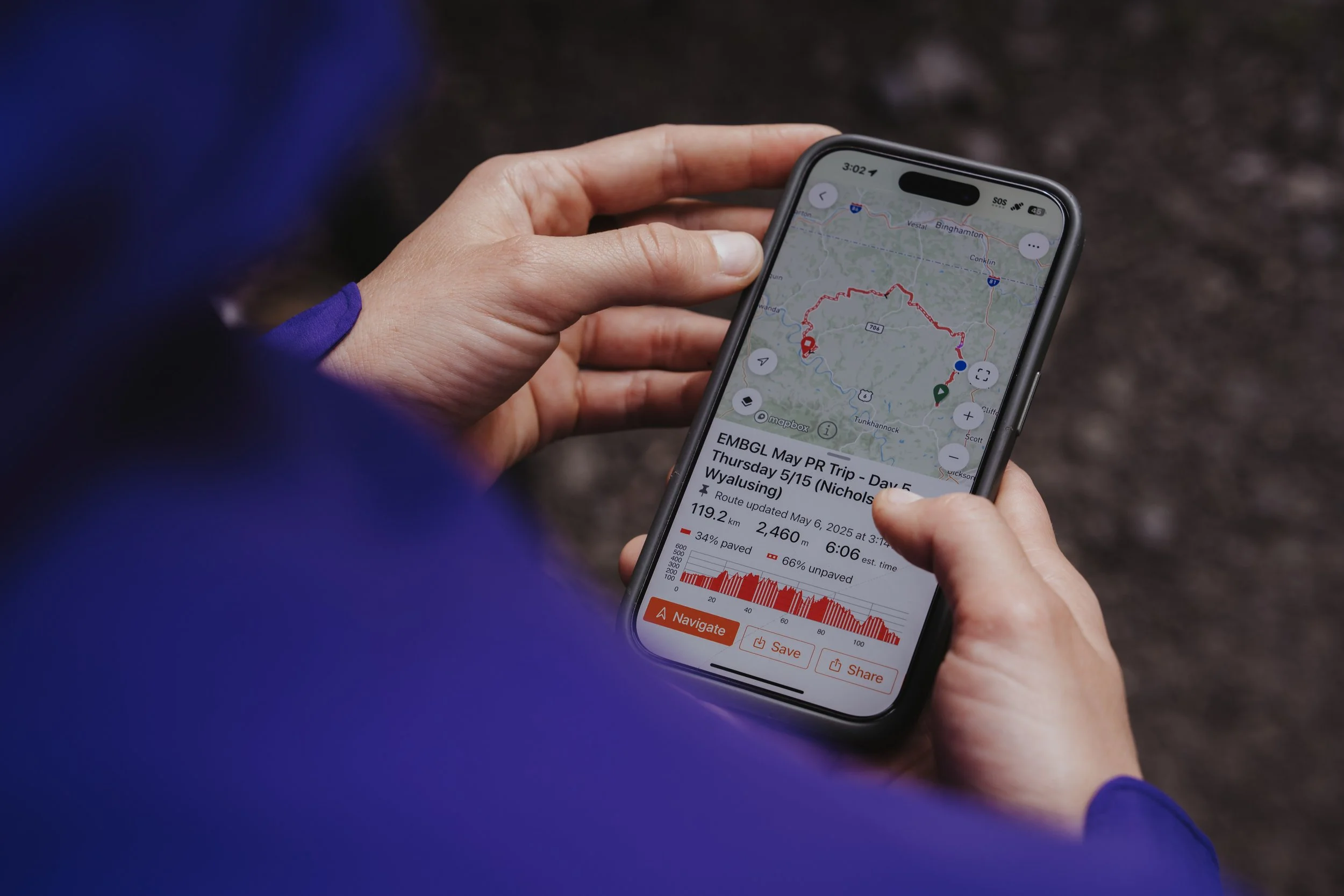 Close-up of a person holding a smartphone displaying a GPS map and route details for a hiking trip, outdoors on a trail.