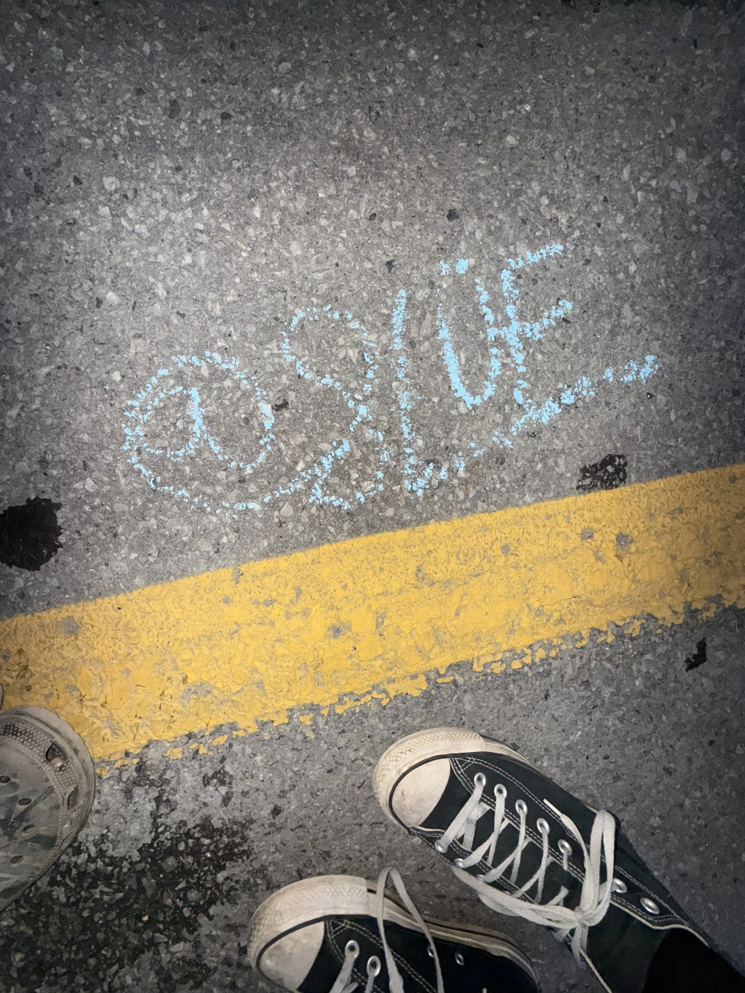 The word 'Blue' is written in blue chalk on the asphalt ground, with a yellow parking line below and sneakers visible at the bottom of the image.