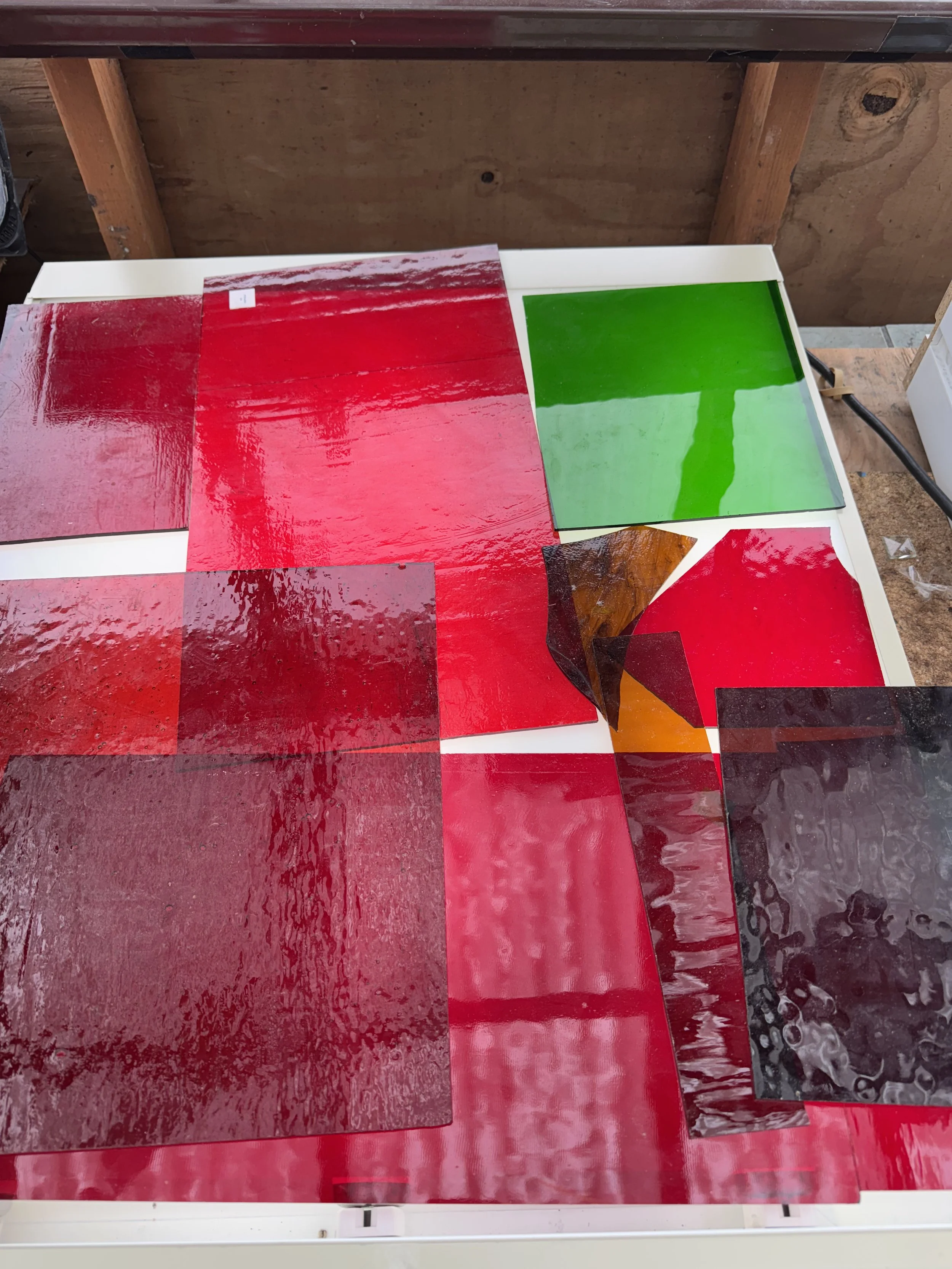 Various sheet materials, including red, green, black, and brown glossy sheets, arranged on a white table in a workshop.