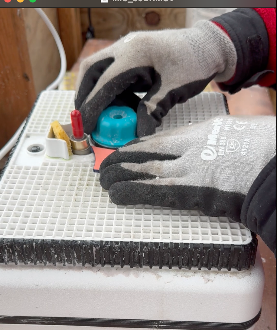 Worker wearing gray gloves assembling or repairing an electronic device on a workbench.