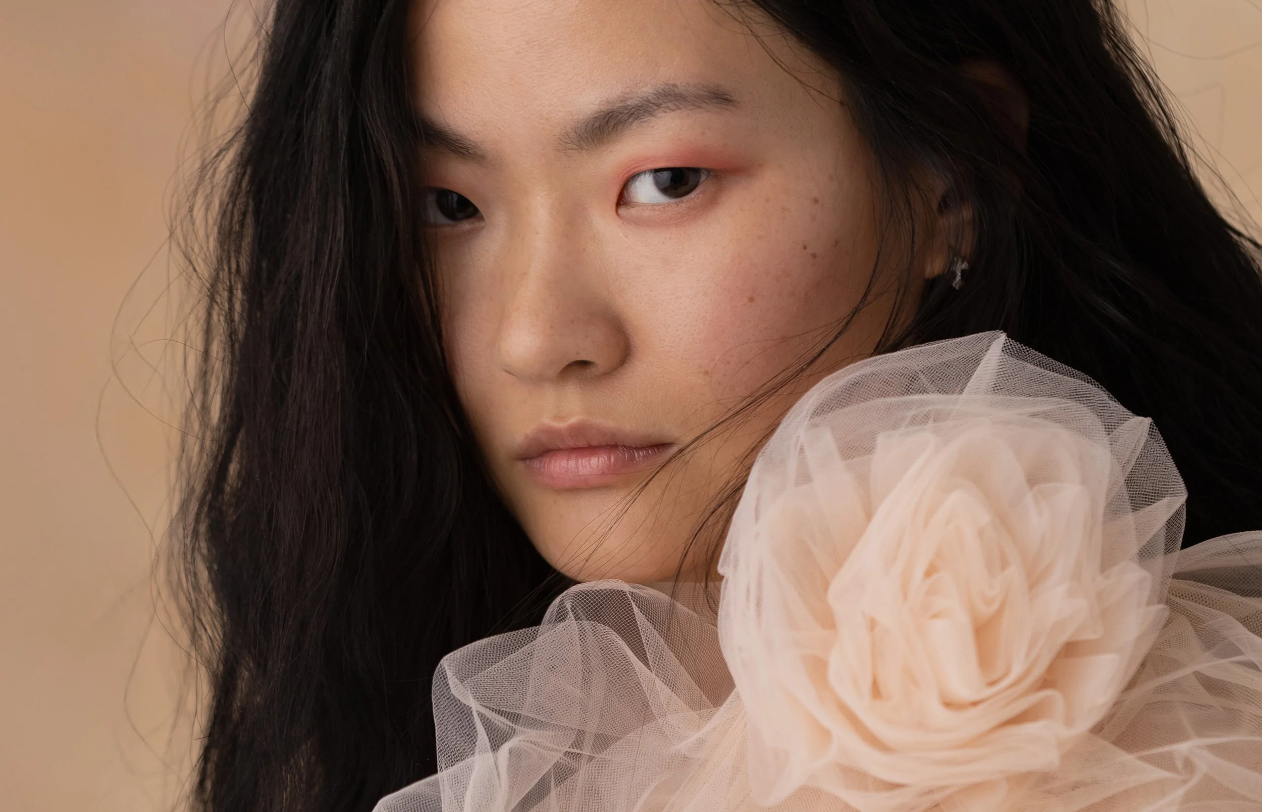 Portrait éditorial de mode d’une femme asiatique dans une lumière douce avec une fleur de tulle poudrée.