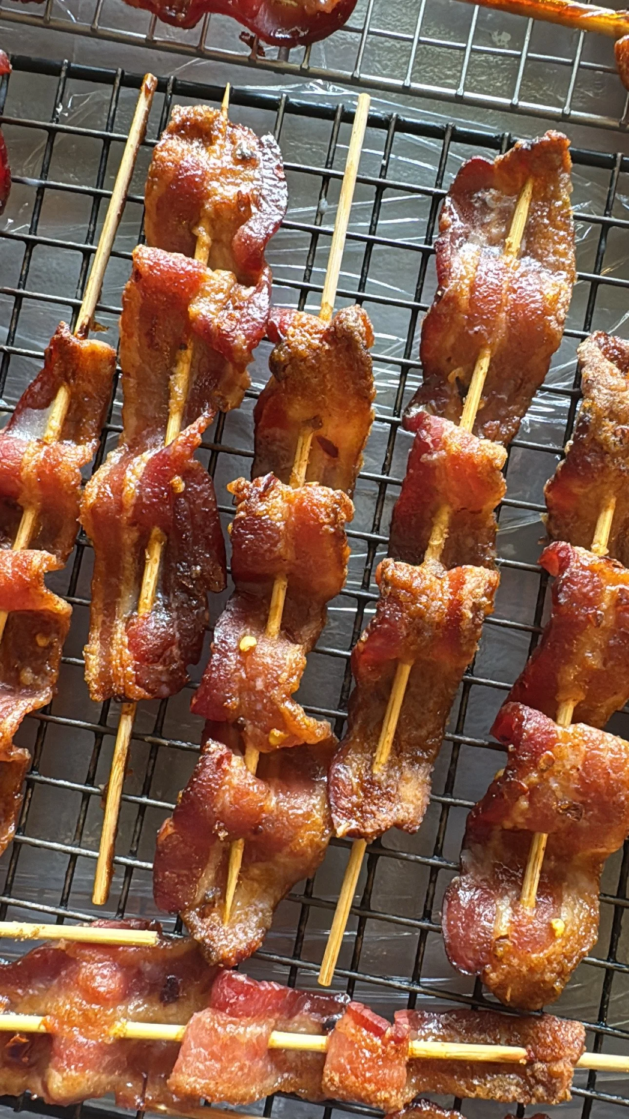Several pieces of bacon wrapped around skewers, cooked on a grill.
