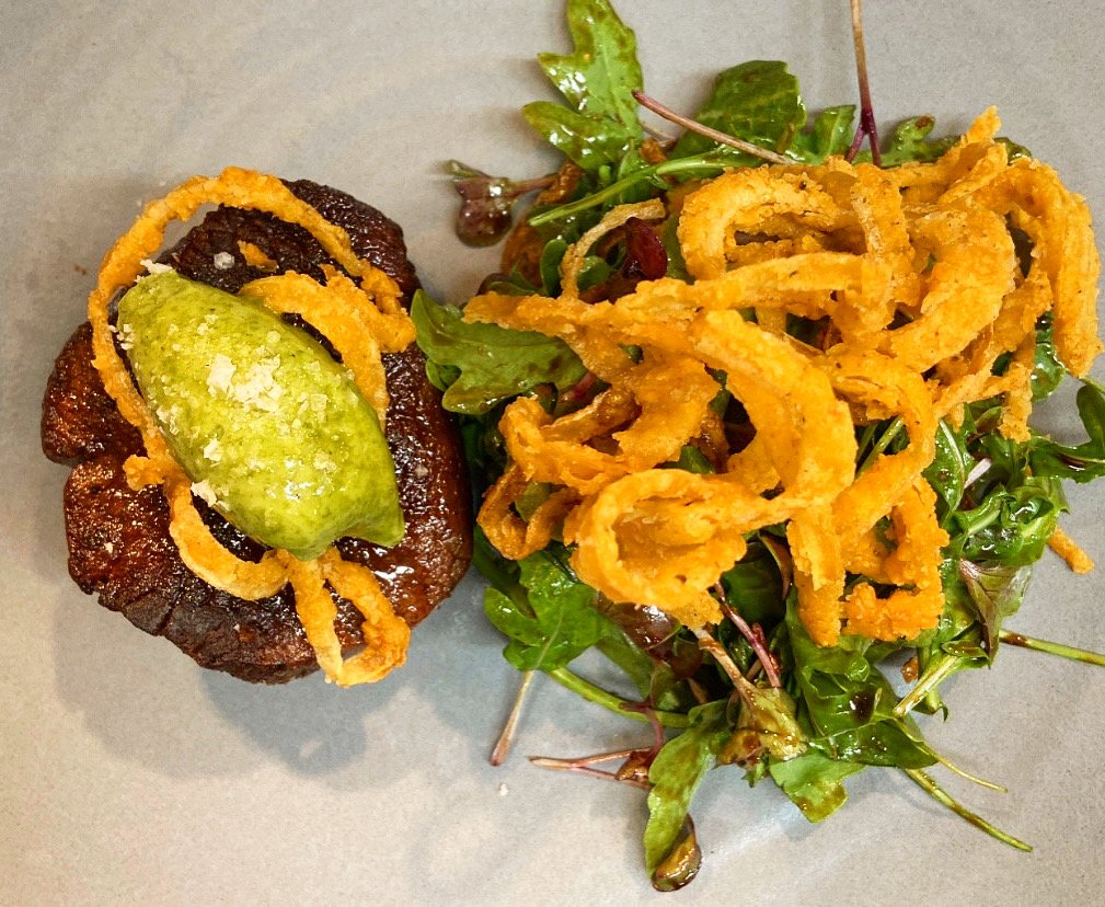 Fried onion rings on a bed of mixed greens with a ketchup and lime dipping sauce.