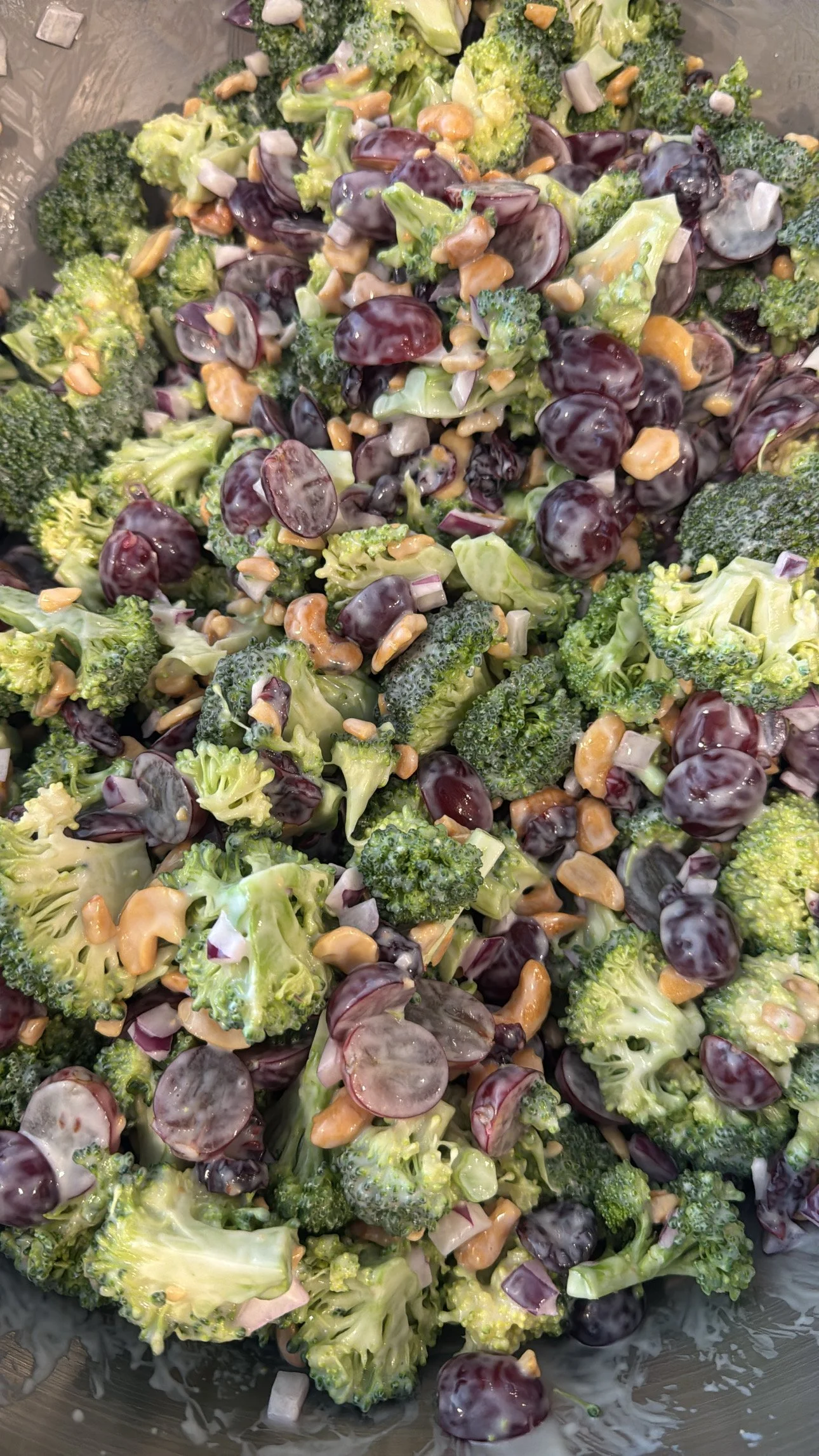 A bowl of broccoli, purple grapes, chopped onions, and crushed nuts salad with a creamy dressing.