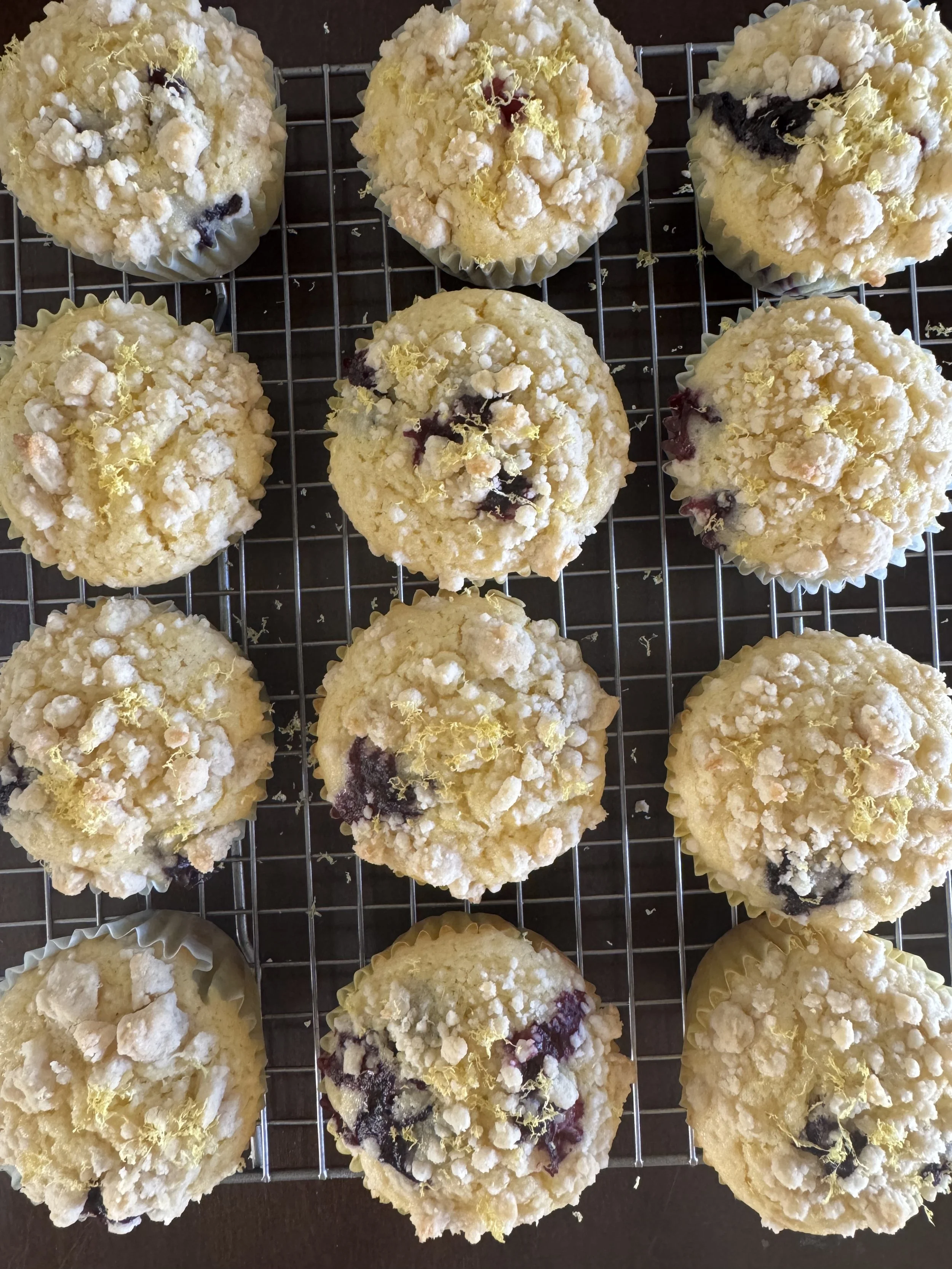 Top view of multiple blueberry crumble muffins on a wire rack, topped with crumbled streusel and lemon zest.